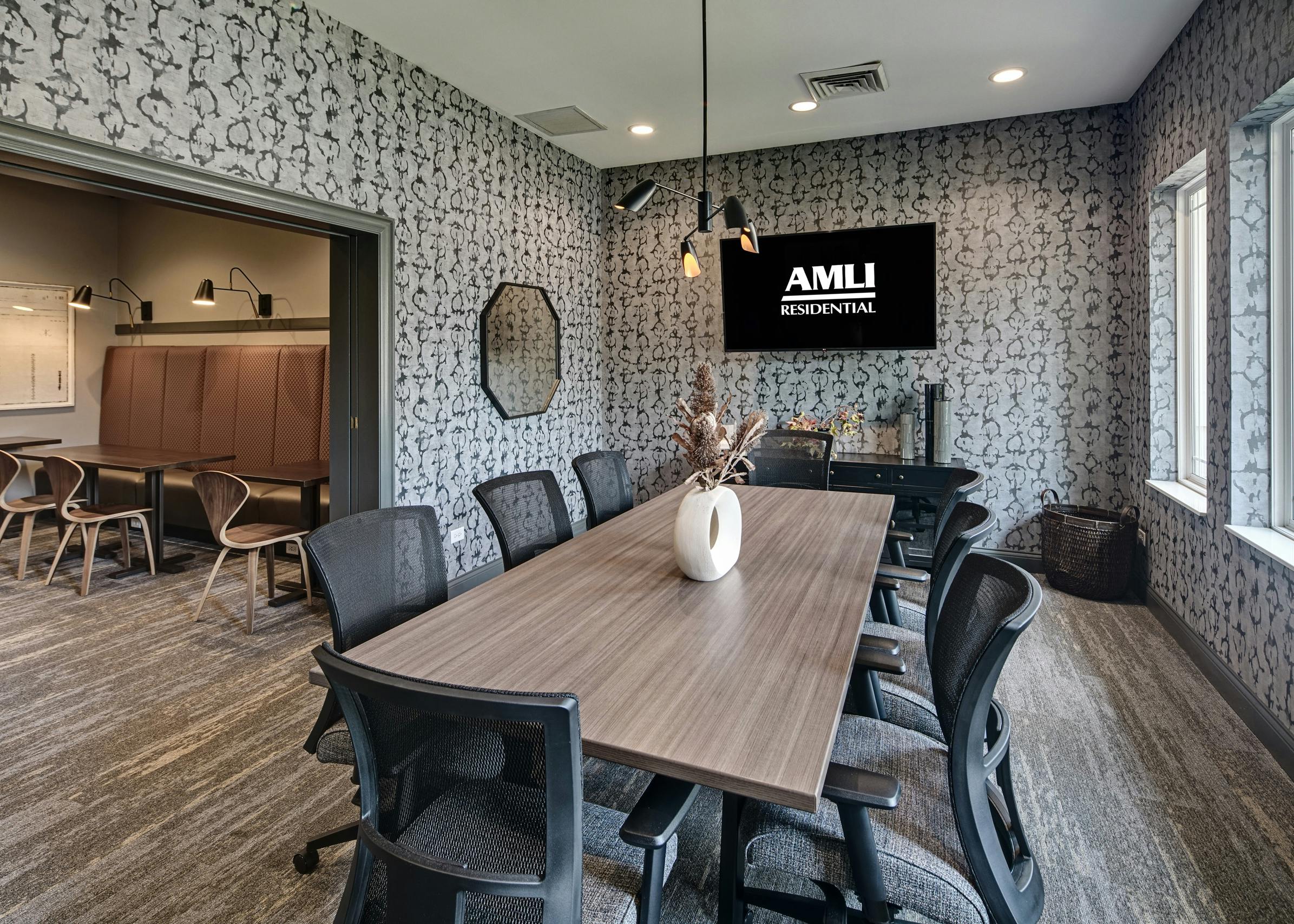 Conference room at AMLI at Seven Bridges apartments with long wood grain table and 8 gray chairs and gray and white wallpaper