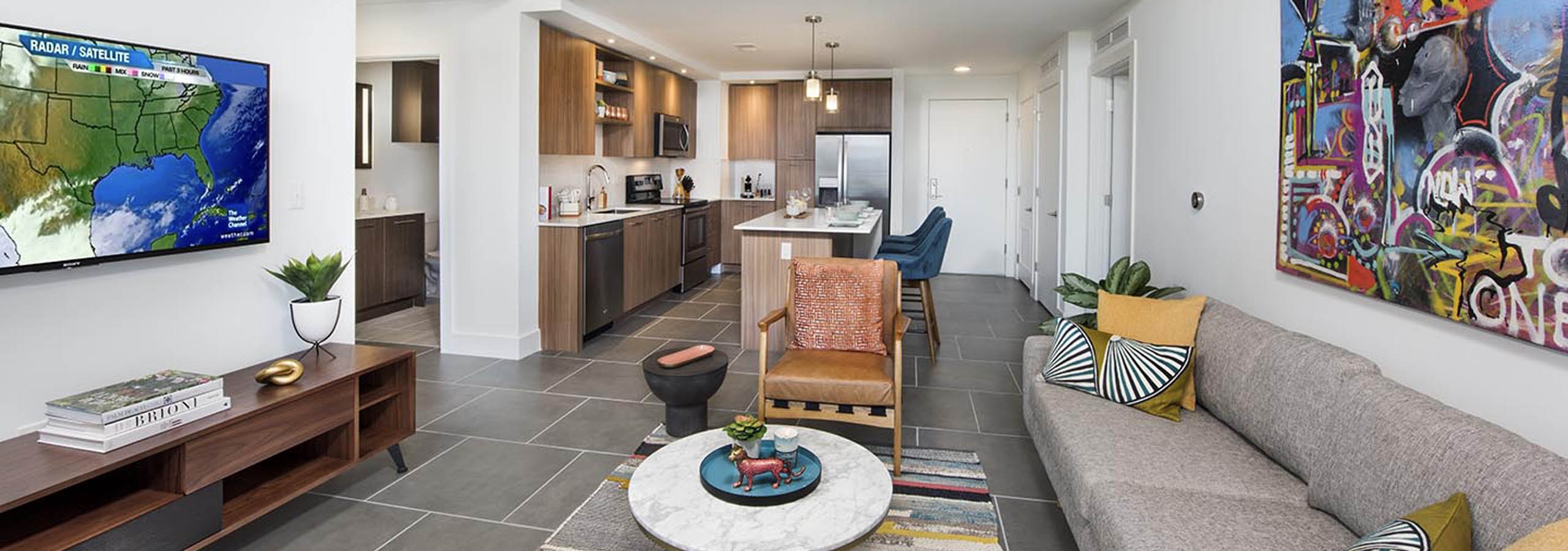 AMLI Midtown 29 living room with grey couch and multi-color artwork on wall with TV and view into kitchen with island
