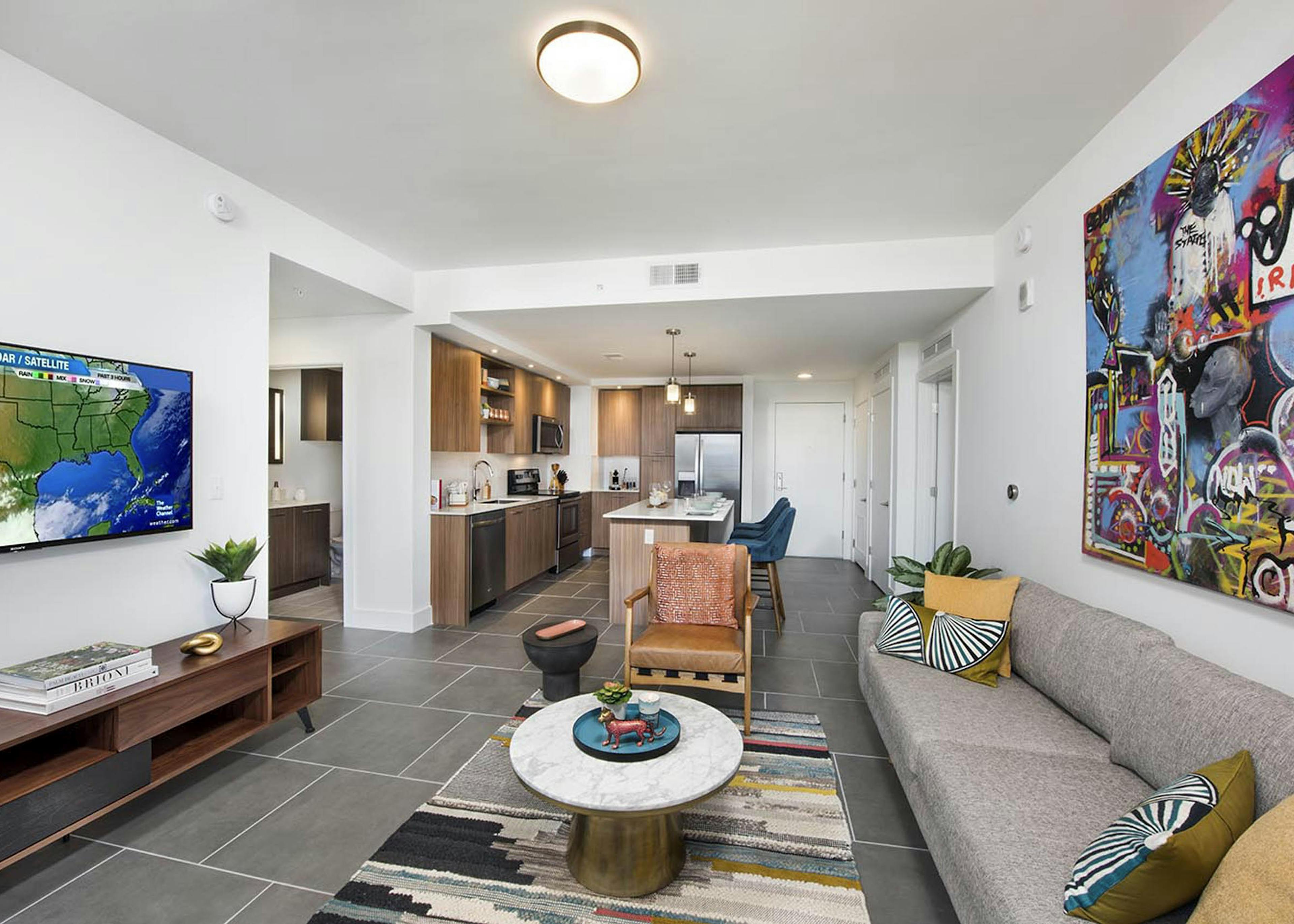 AMLI Midtown 29 living room with grey couch and multi-color artwork on wall with TV and view into kitchen with island