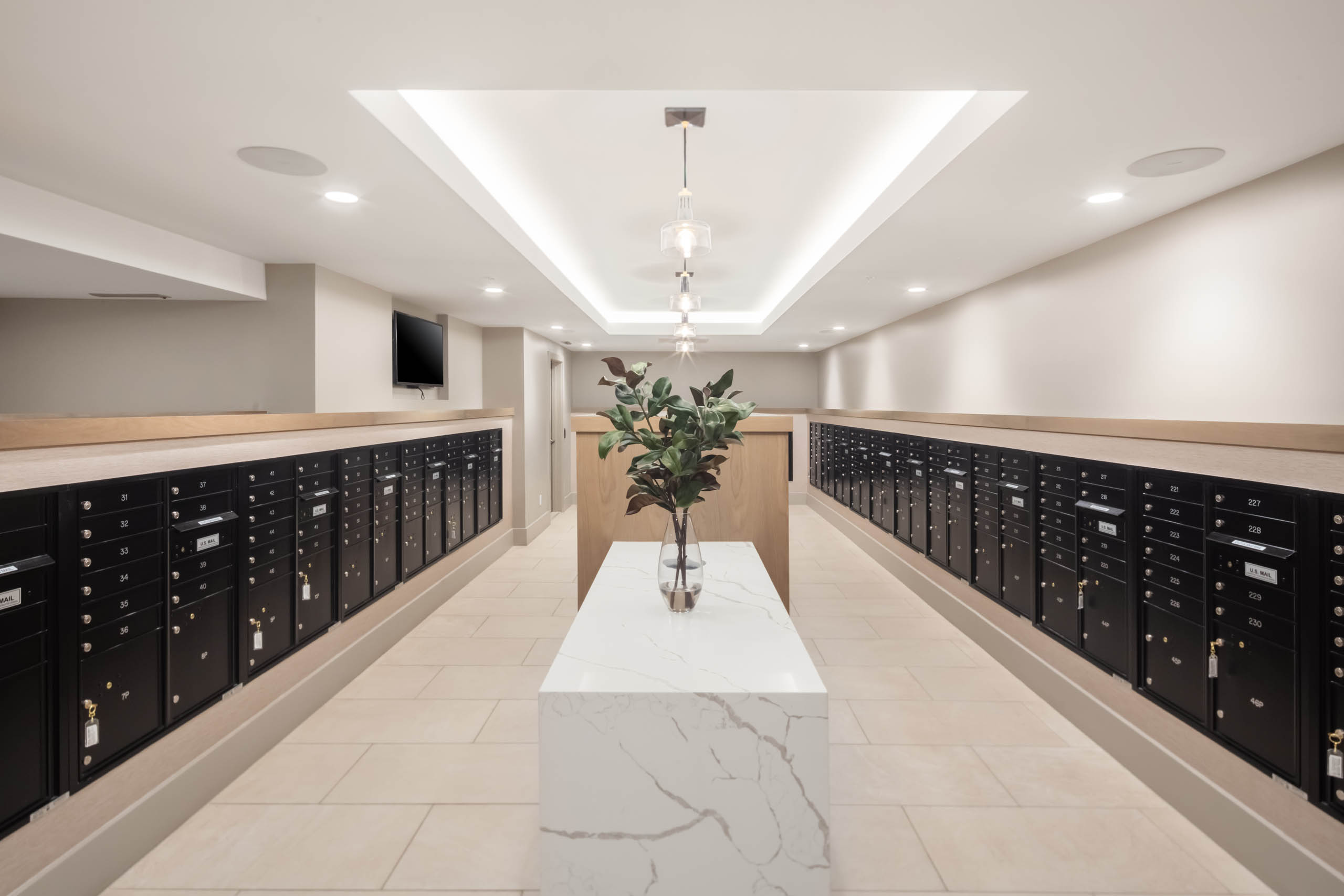 Greenery in a clear vase resting on a marble table in the center of the AMLI at Uptown mailroom lined with black mailboxes
