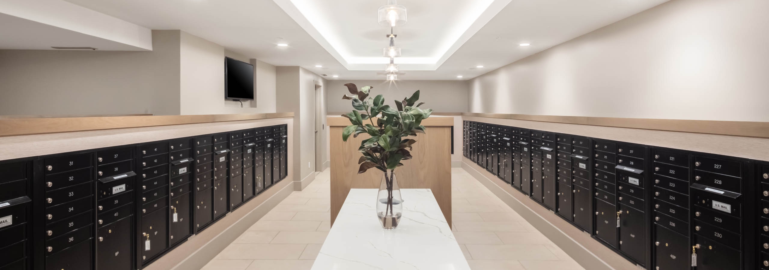 Greenery in a clear vase resting on a marble table in the center of the AMLI at Uptown mailroom lined with black mailboxes