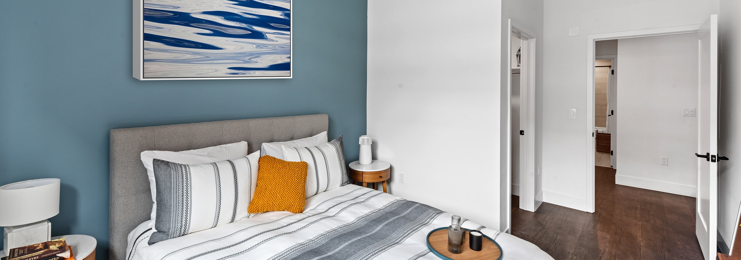 Spacious bedroom with blue accent wall and nightstands facing towards closet and bathroom at AMLI Old Pasadena apartments