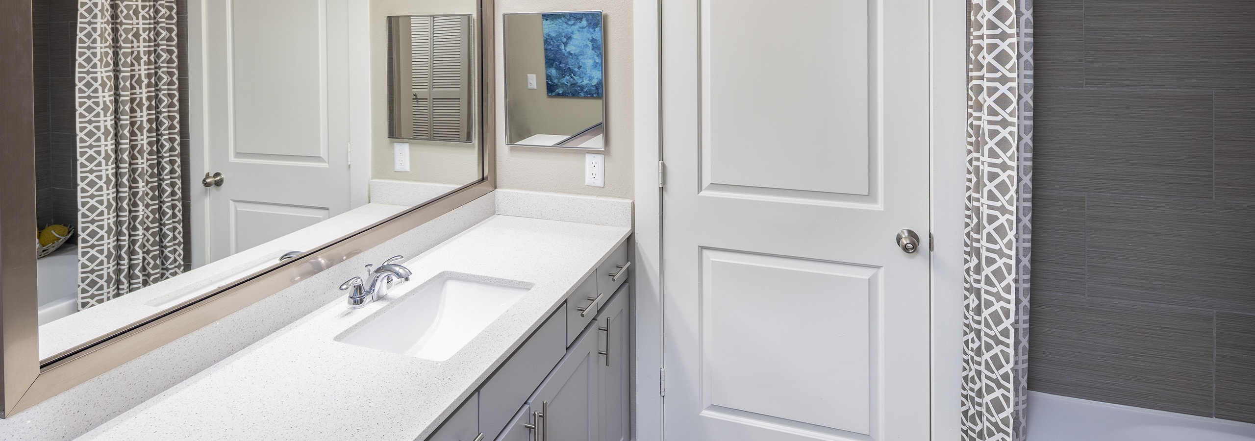 AMLI Eastside apartment bathroom featuring gray vanity with white quartz countertops and white bathtub with brown surround