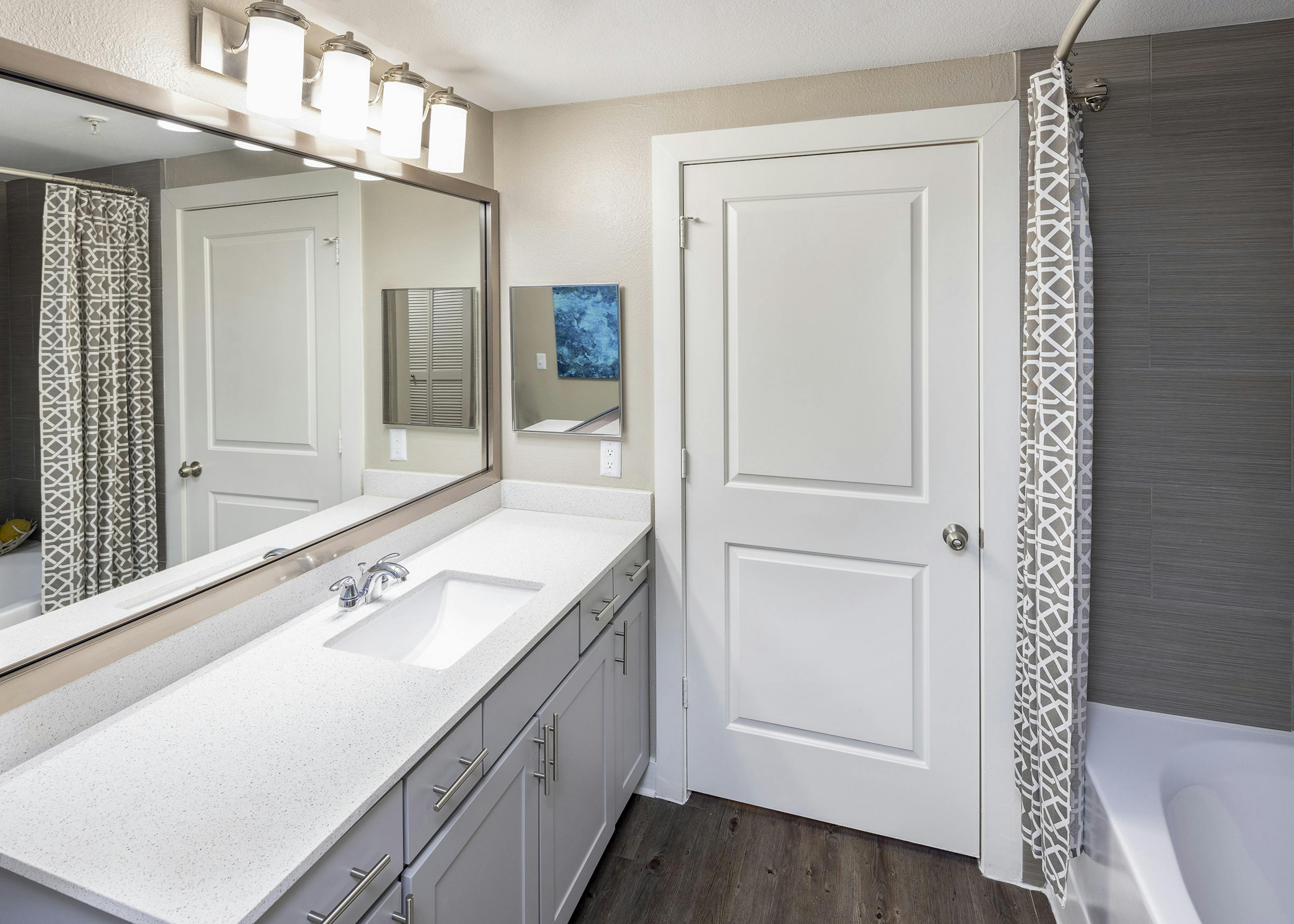 AMLI Eastside apartment bathroom featuring gray vanity with white quartz countertops and white bathtub with brown surround