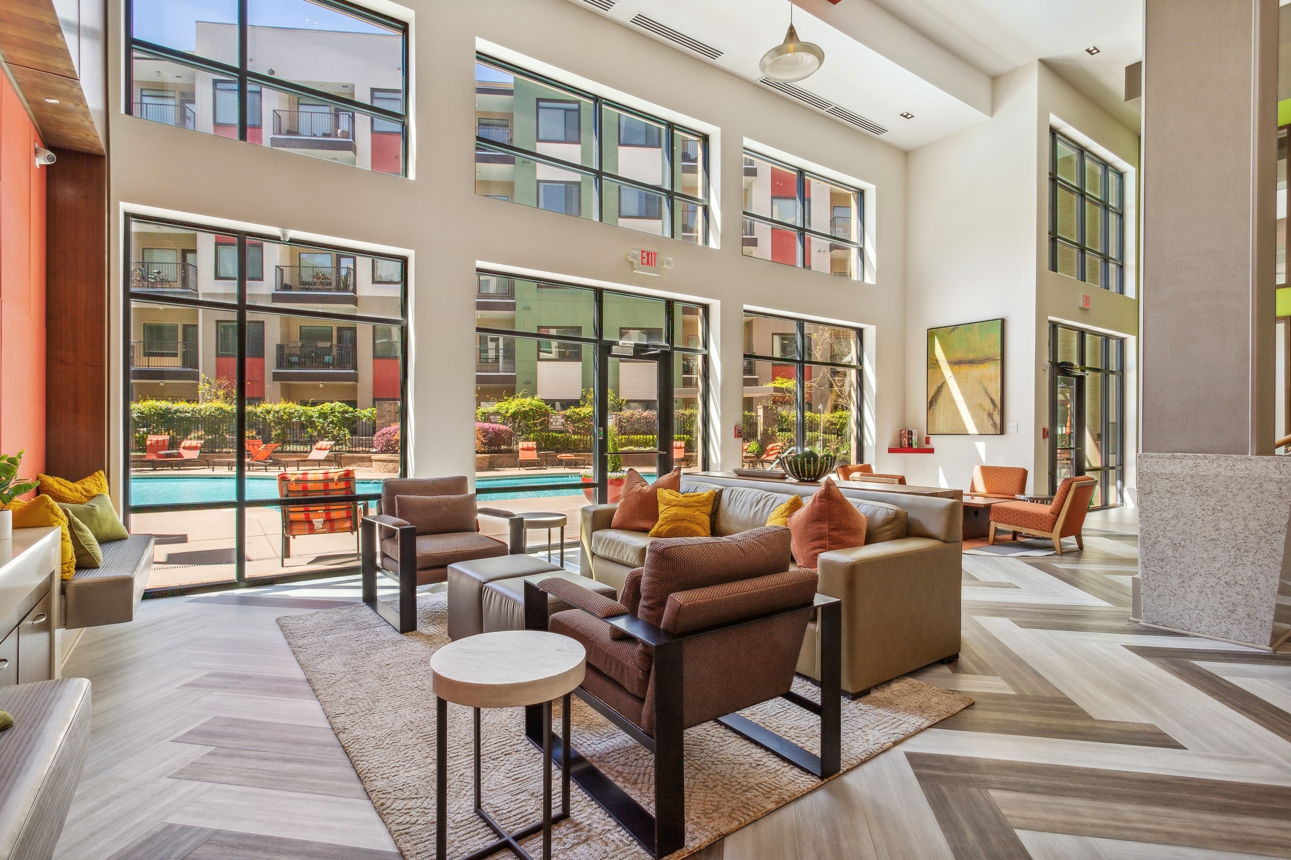 Two-story clubroom with various comfortable seating with pillows and large windows looking out the courtyard pool