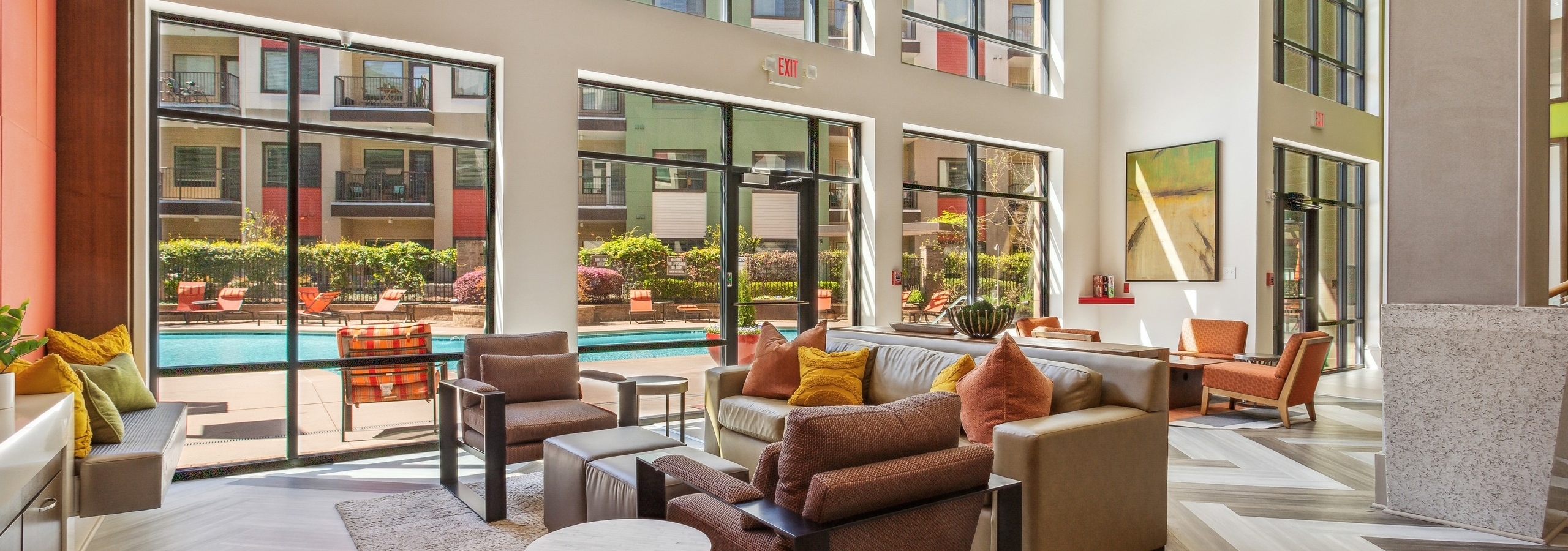 Two-story clubroom with various comfortable seating with pillows and large windows looking out the courtyard pool