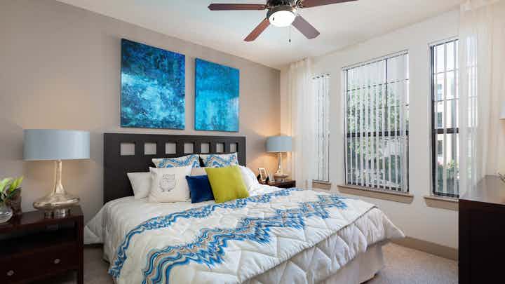 AMLI Eastside bedroom with bright windows and vibrant blue wall art hanging on a tan accent wall above a white bed
