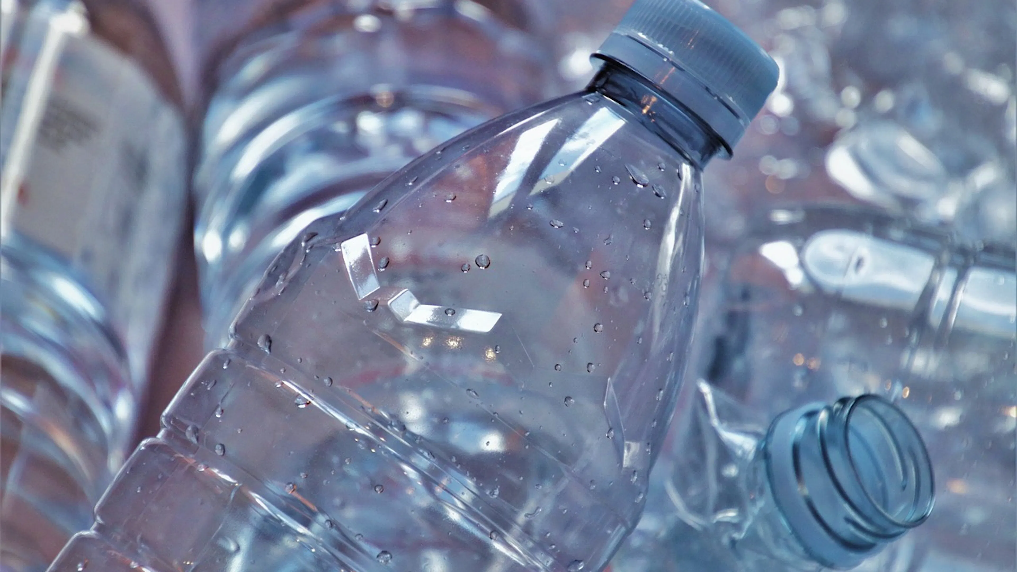 A close up of a clear plastic water bottle in a pile of other empty bottles