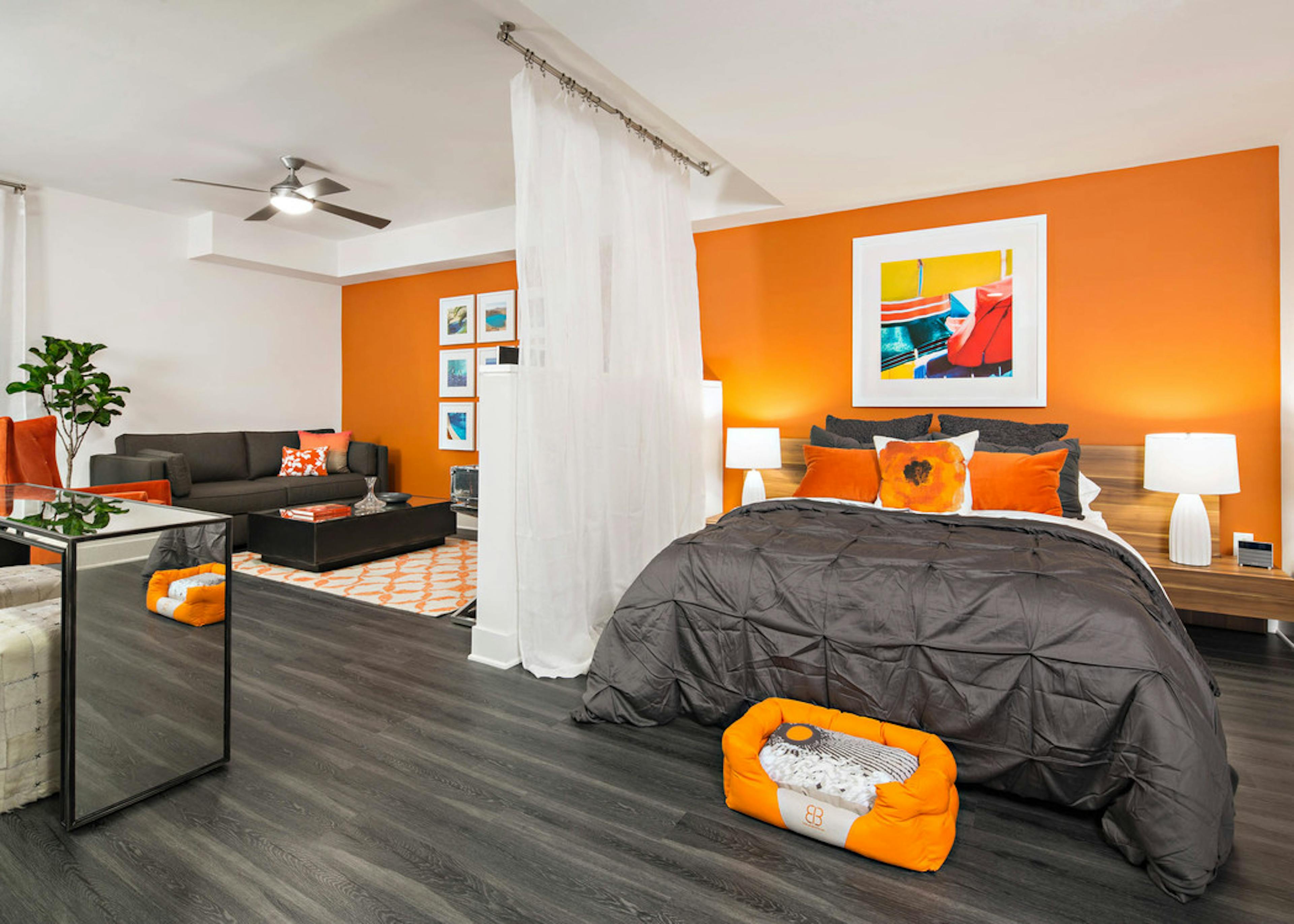 Interior of AMLI Lex on Orange furnished studio apartment with orange wall, queen bed, gray couch and coffee and dining table