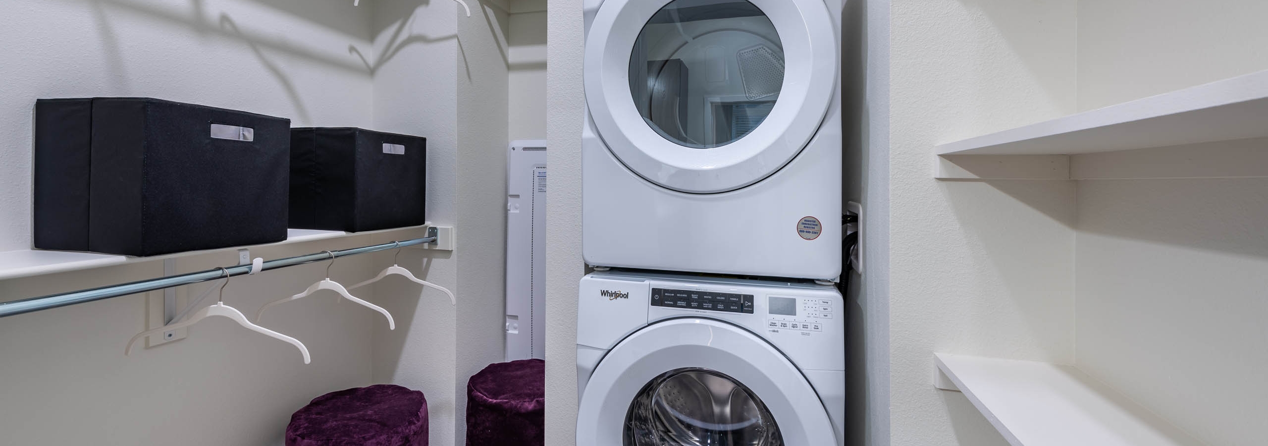 Interior view of a laundry room at AMLI Art District showcasing a stacked washer and dryer and two closet rods with hangers