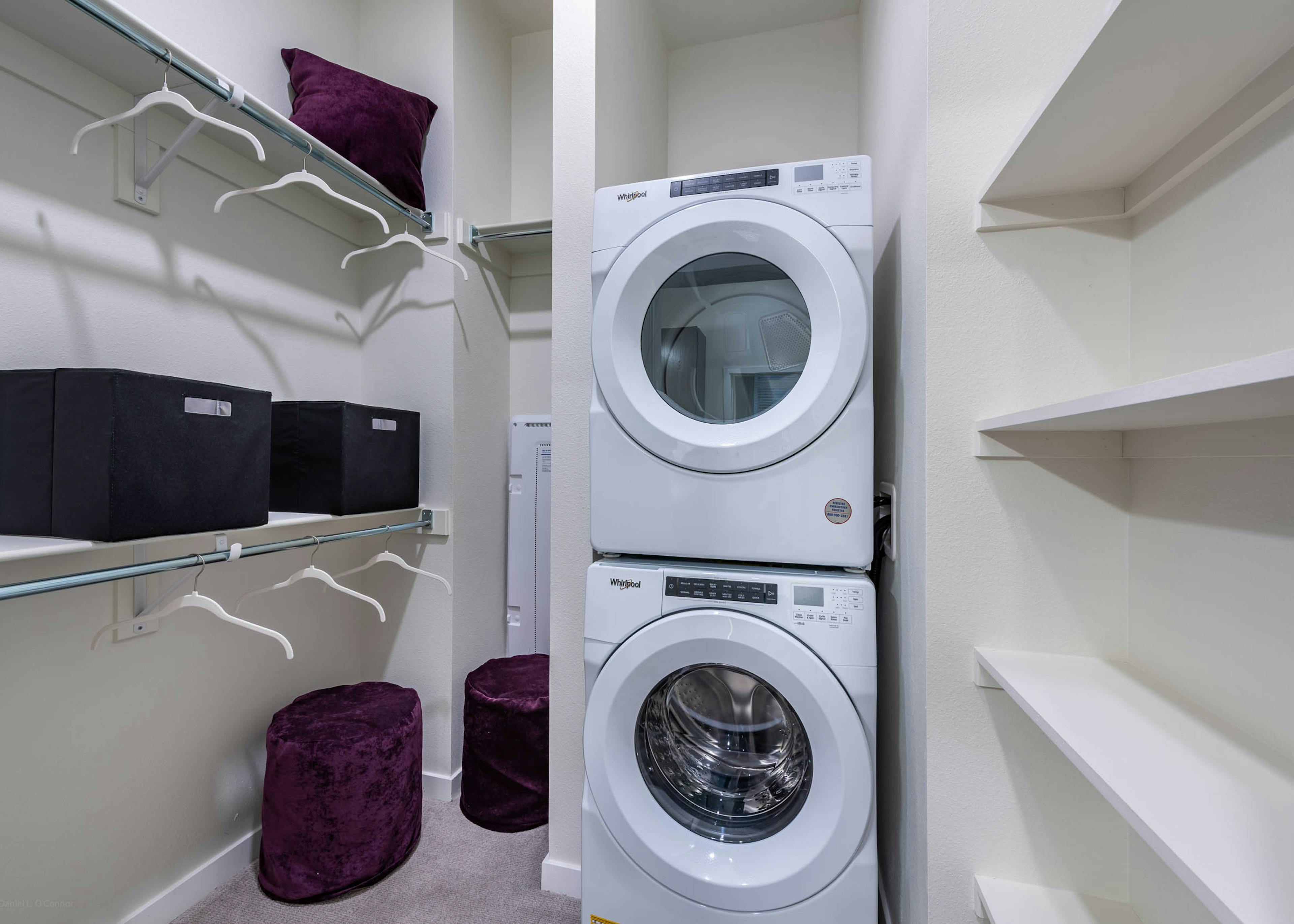 Interior view of a laundry room at AMLI Art District showcasing a stacked washer and dryer and two closet rods with hangers