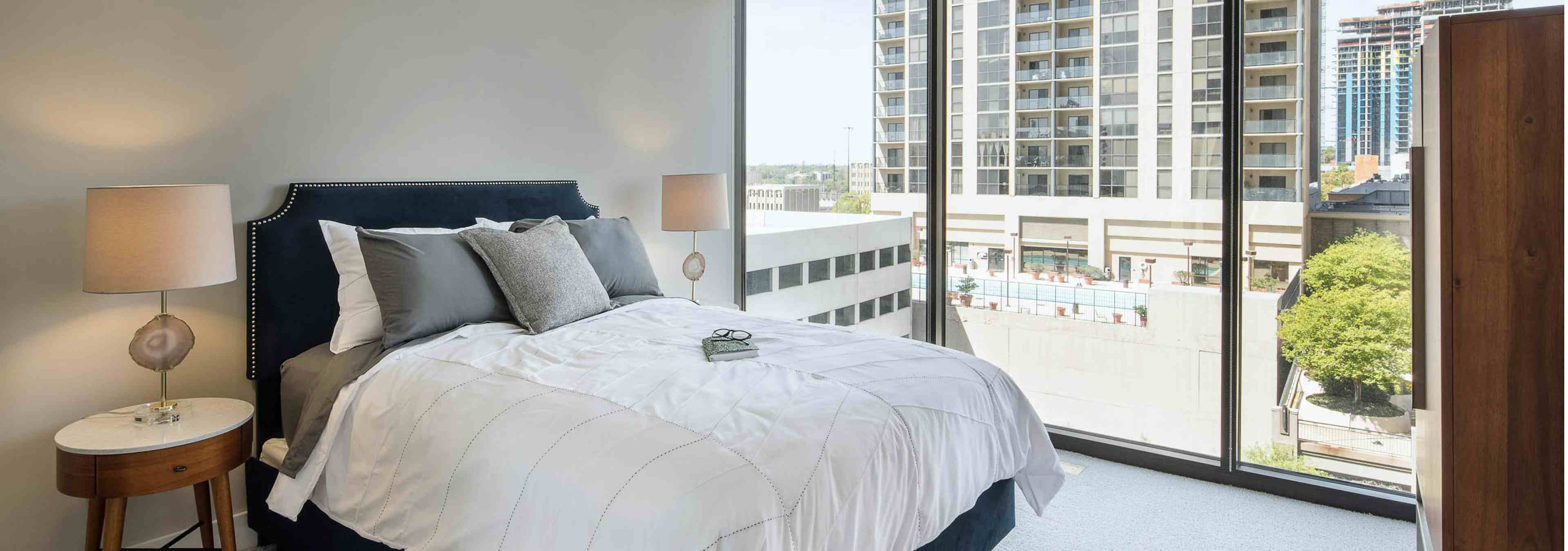 Interior of bedroom at AMLI Arts Center with grey and white bedding and floor to ceiling windows with a daytime city view