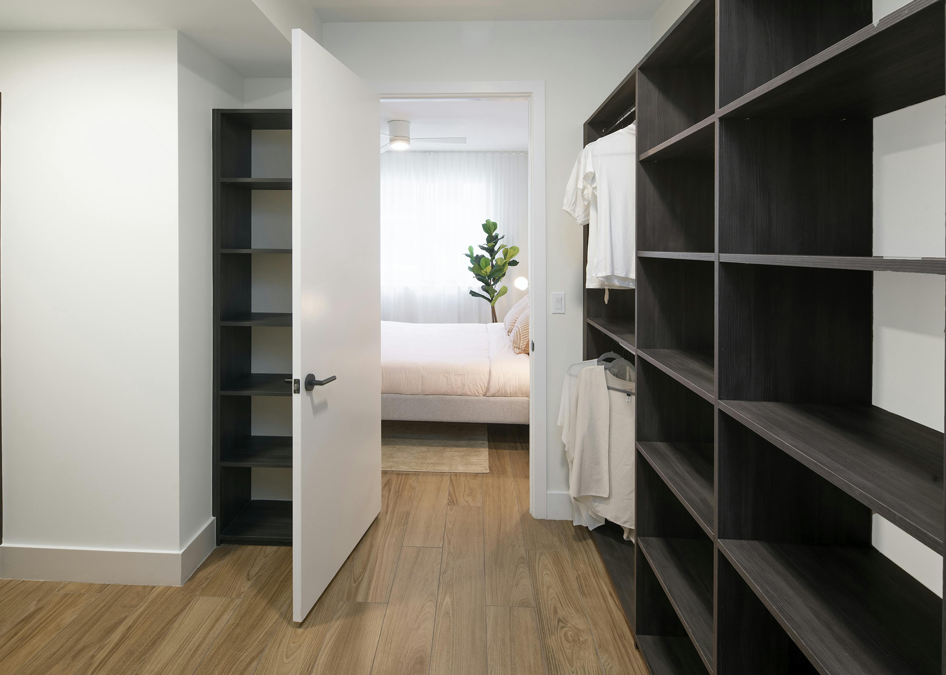 AMLI Midtown Miami apartment large walk in closet with dark wood shelving and plank wood floors and peek into bedroom