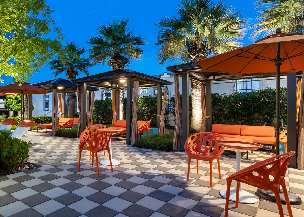 Cabanas at the AMLI on Riverside pool with covered orange chairs and couches and a nighttime view of palm trees in the background