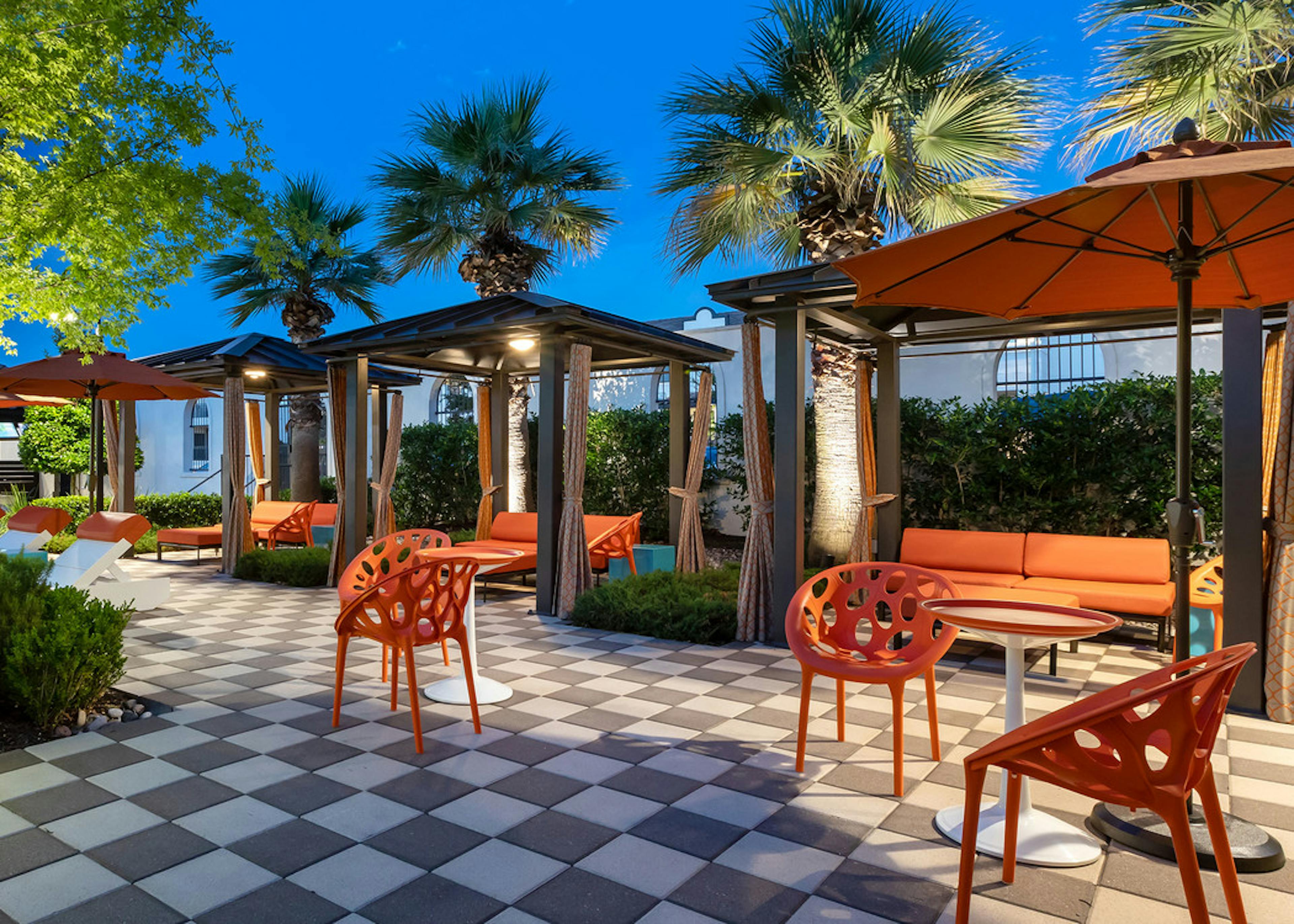 Cabanas at the AMLI on Riverside pool with covered orange chairs and couches and a nighttime view of palm trees in the background