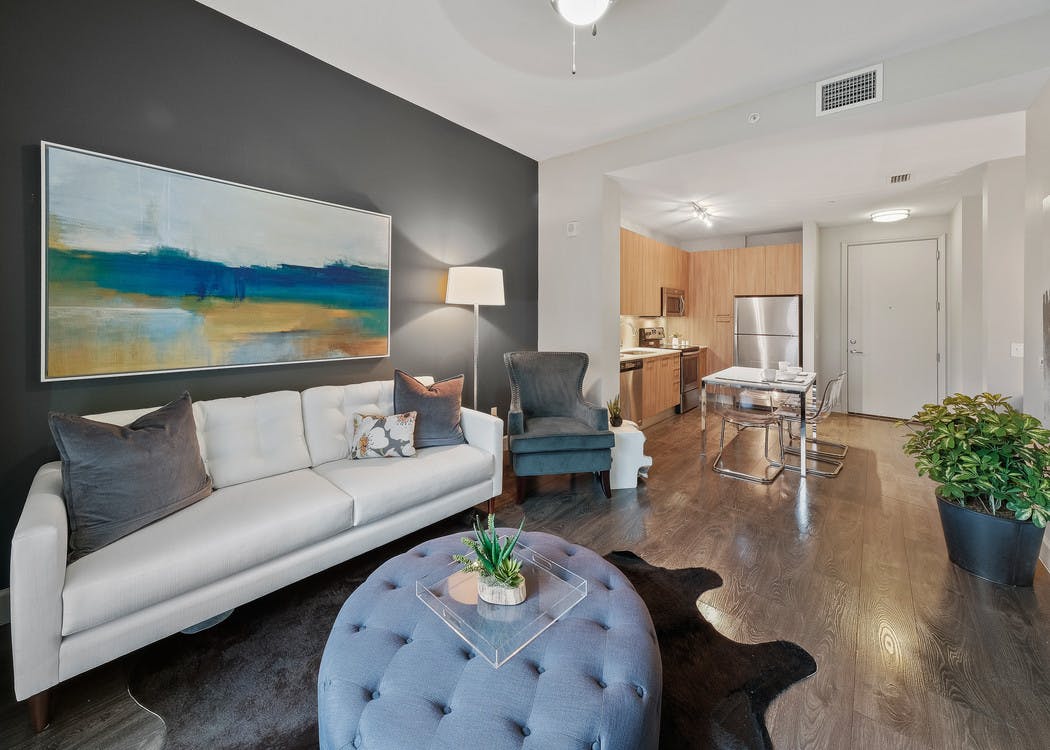 AMLI 8800 apartment living area with white sofa and artwork with blue shoes, toss pillows and a peek into the kitchen