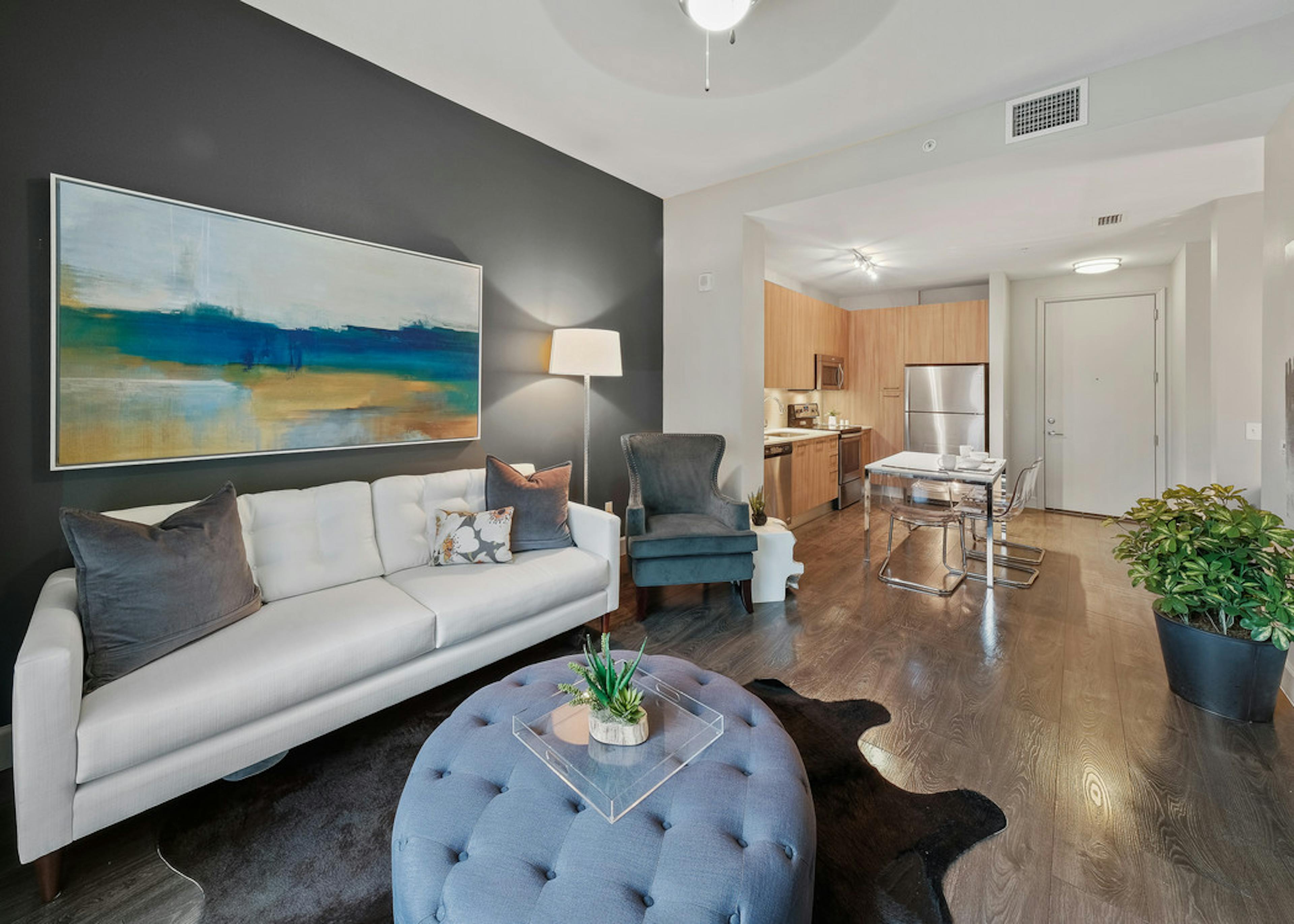 AMLI 8800 apartment living area with white sofa and artwork with blue shoes, toss pillows and a peek into the kitchen 