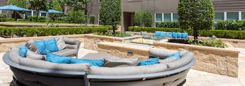 Daytime view of landscaped courtyard at AMLI River Oaks apartments with a double-sided fire pit and comfortable seating