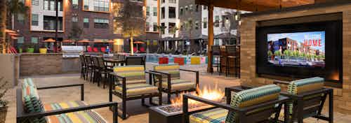AMLI on Aldrich outdoor living area with colorful seating around a fire facing large TV with build facade in background