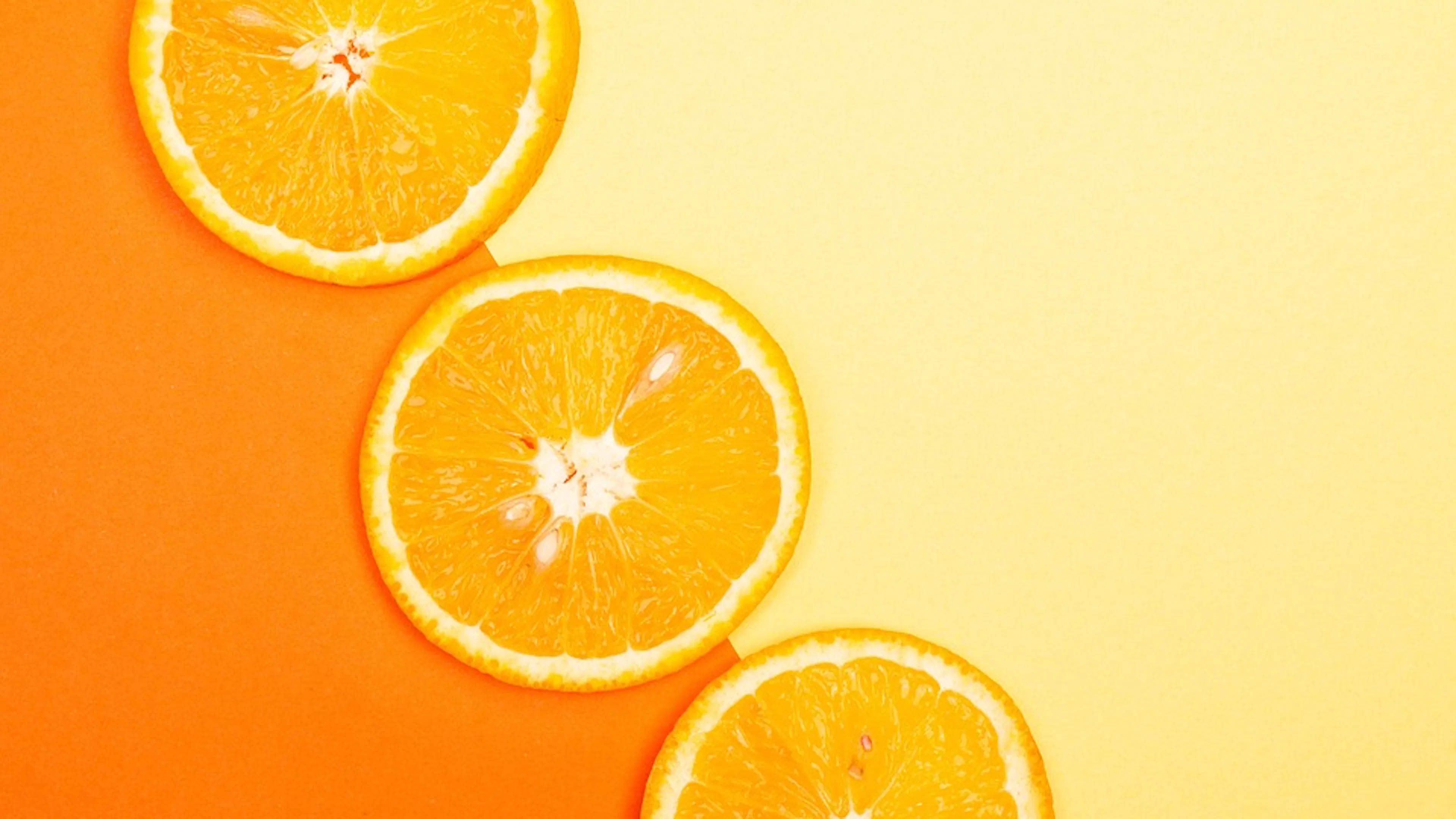 Three orange slices laid diagonally next to each other over a yellow and orange striped background