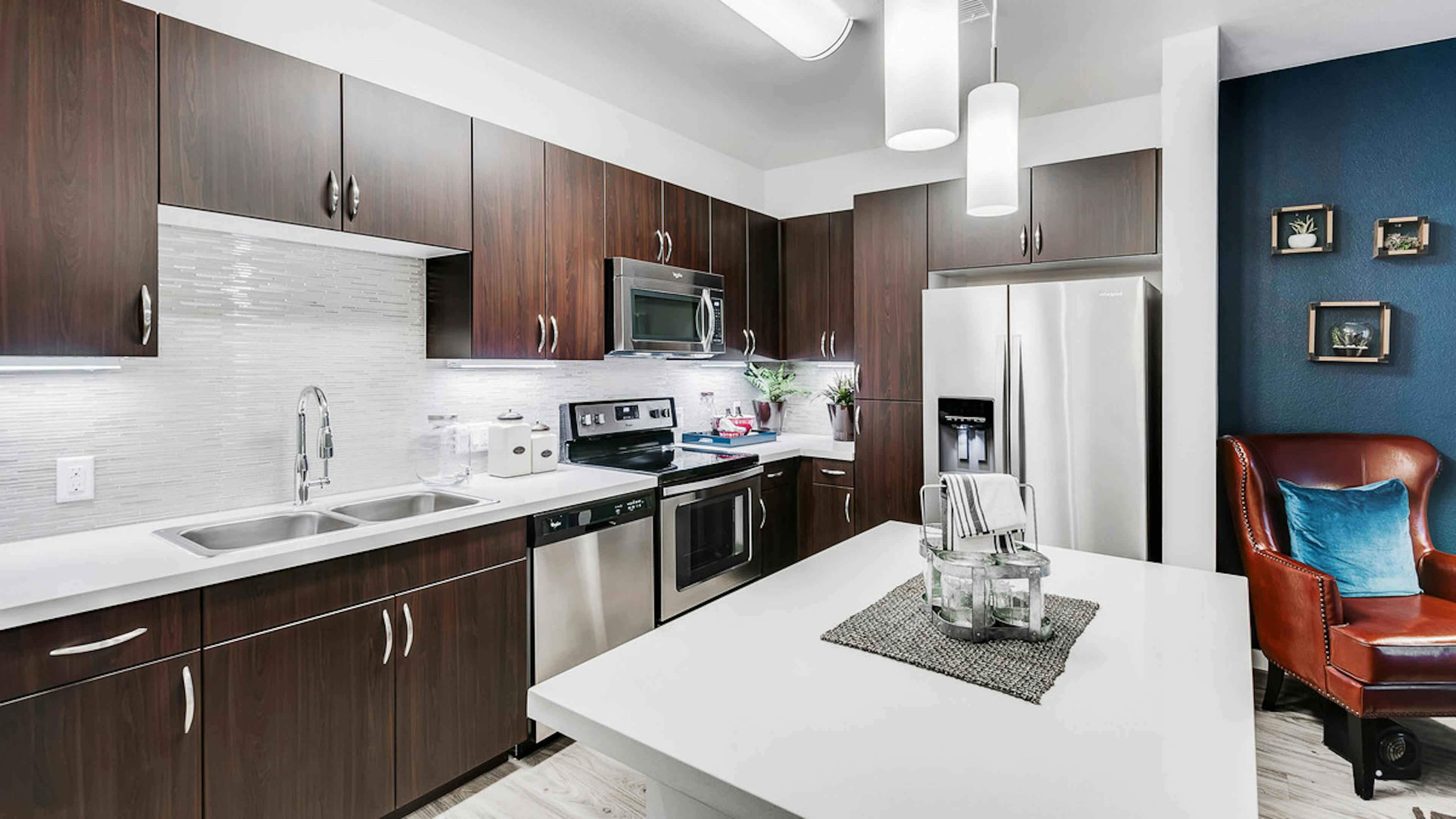 Interior view of a kitchen at AMLI Cherry Creek apartments with an island and white granite counter top and living room chair