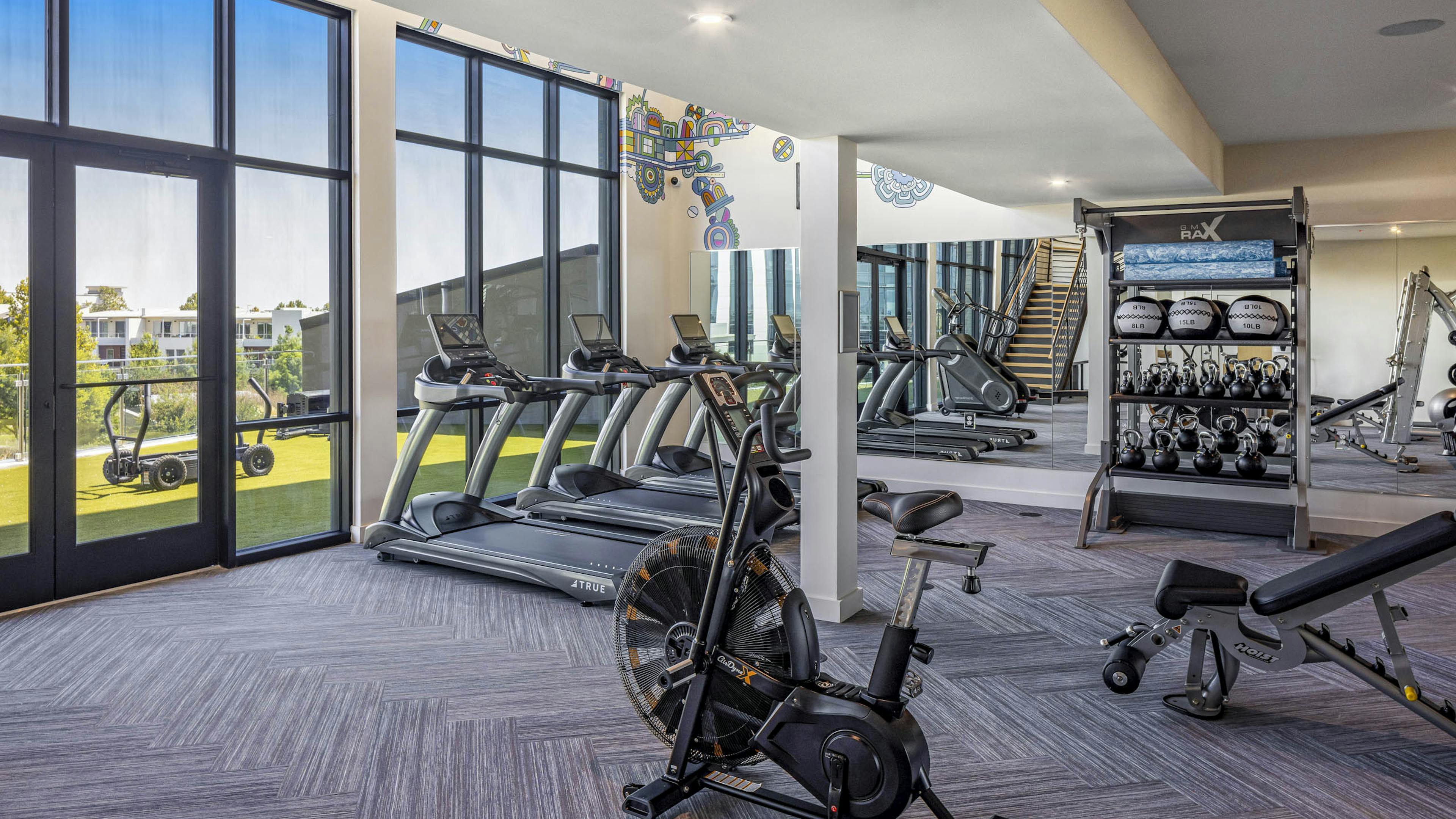 AMLI Branch Park fitness center with weathered grey floor and treadmills and mirrored wall facing outdoor fitness deck