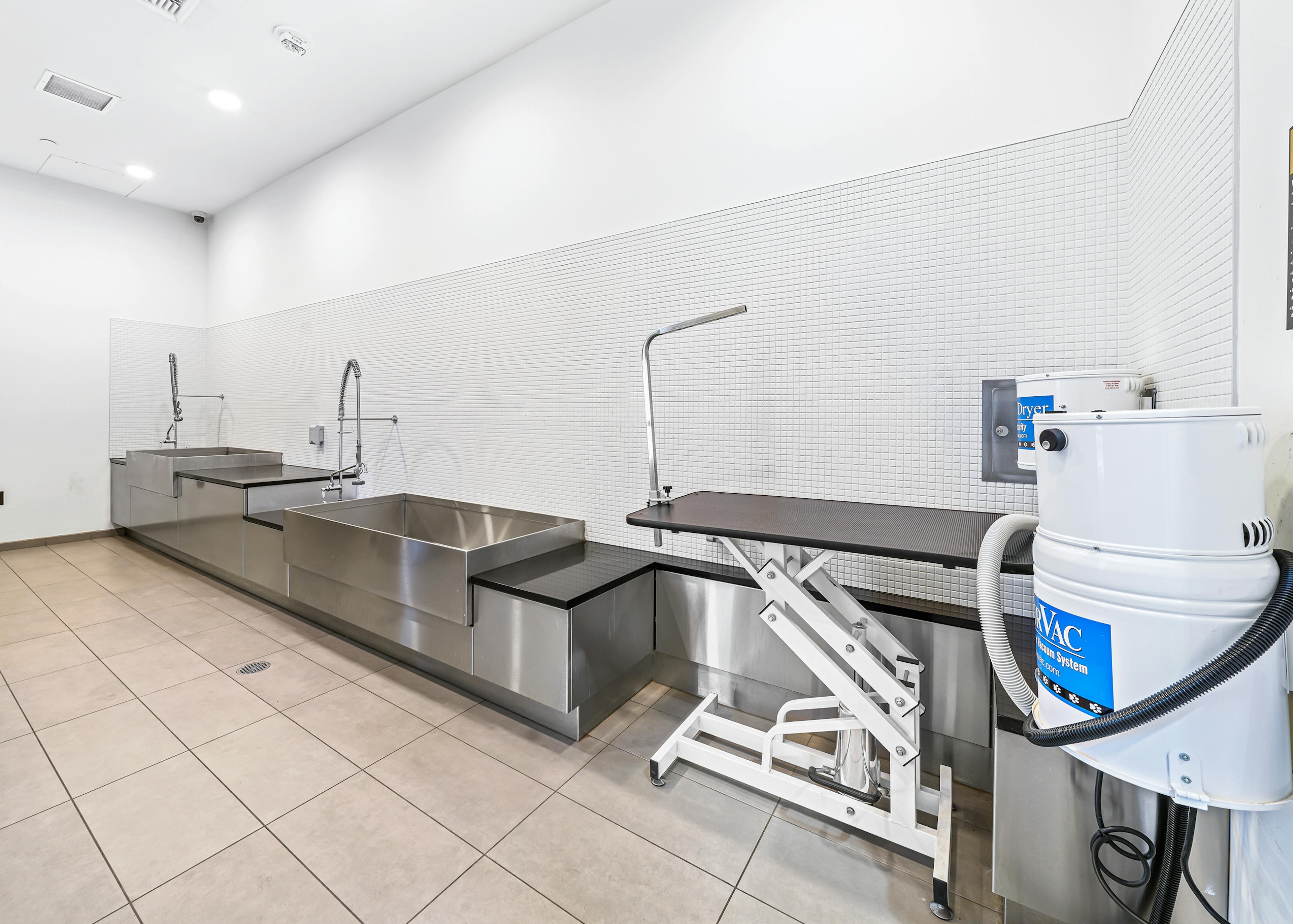Paw wash at AMLI Arc apartment building with 2 sinks with sprayers and a grooming station with dryer against white tiled wall