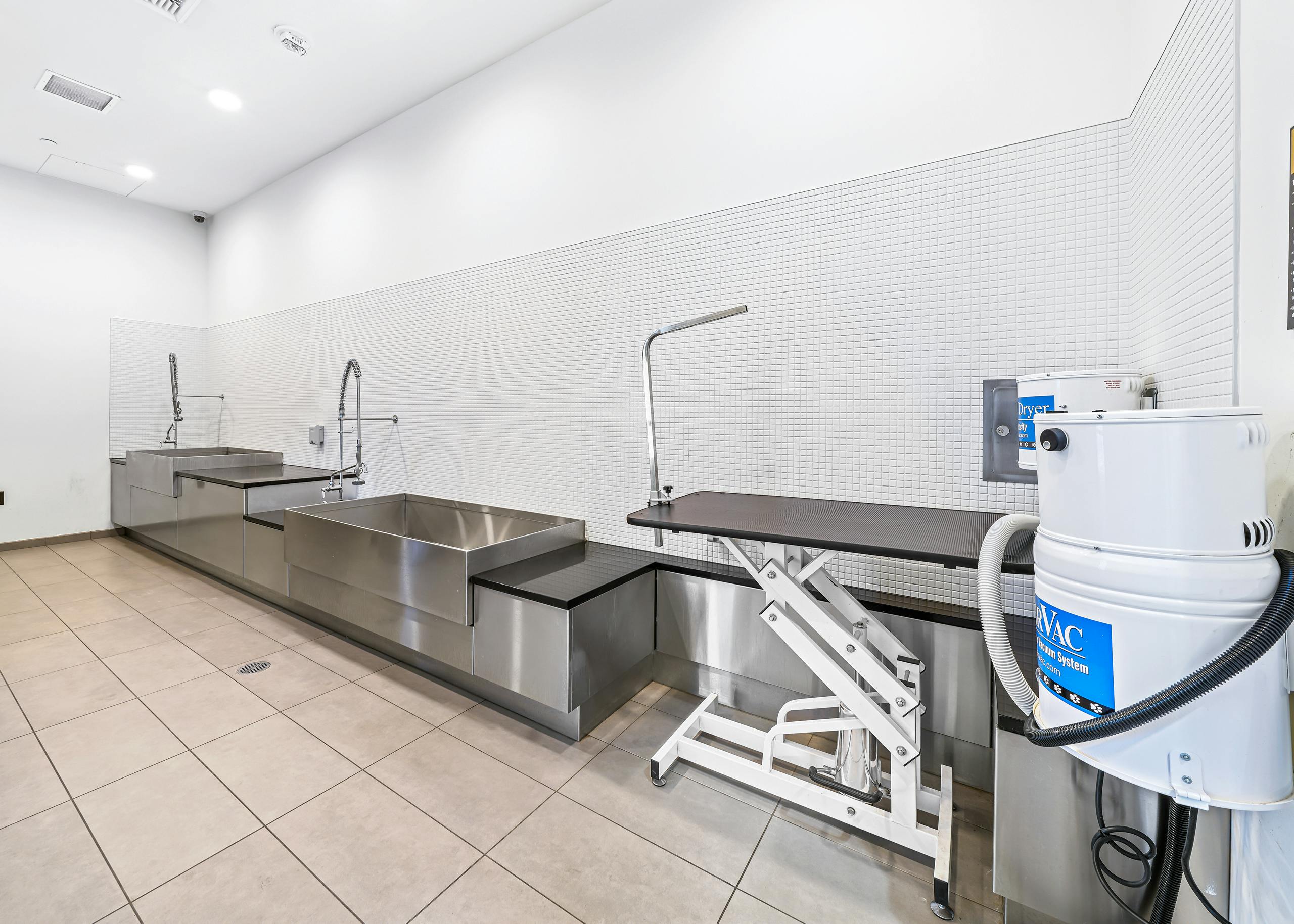 Paw wash at AMLI Arc apartment building with 2 sinks with sprayers and a grooming station with dryer against white tiled wall