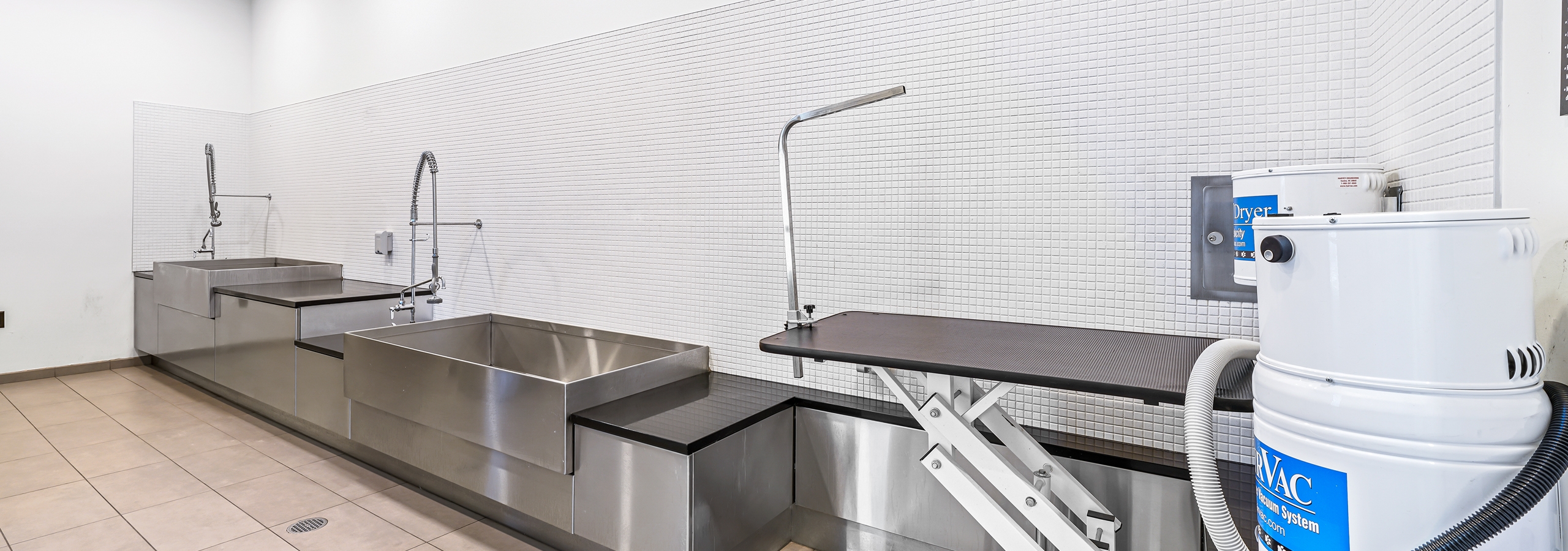 Paw wash at AMLI Arc apartment building with 2 sinks with sprayers and a grooming station with dryer against white tiled wall