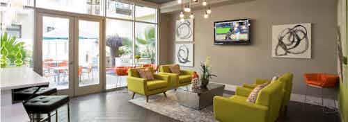 AMLI 5350 resident lounge with dark hardwood and green seating by floor to ceiling windows along a wall with door to patio