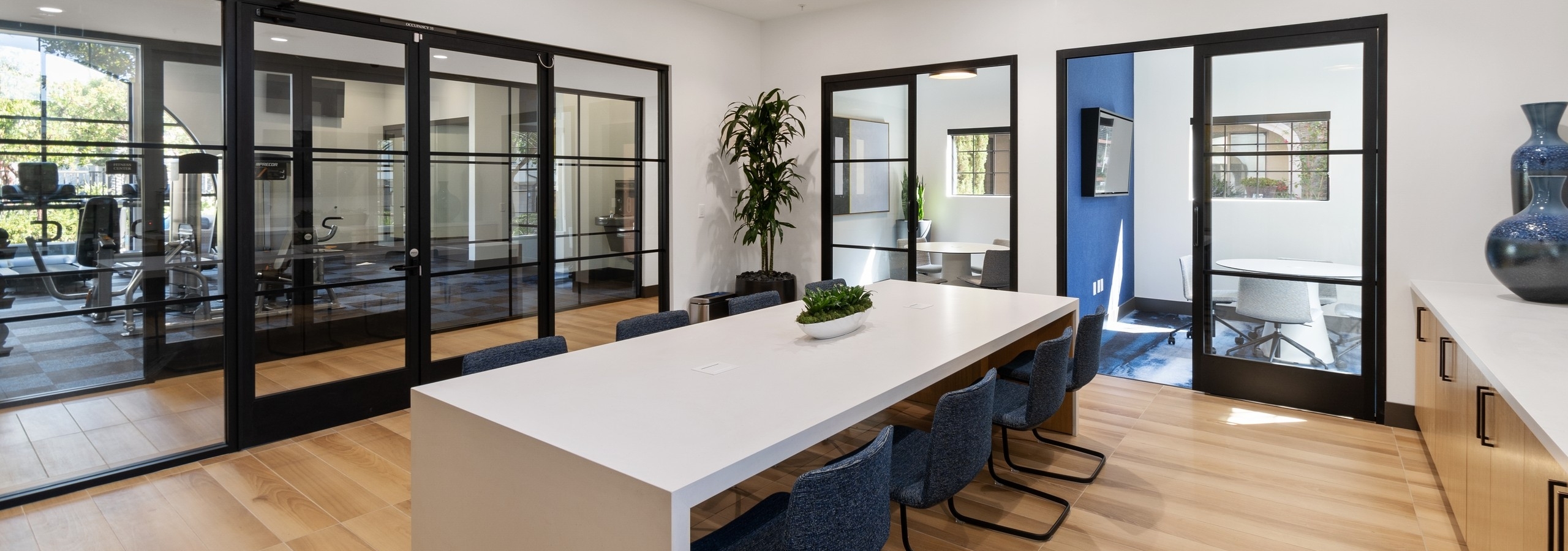 WiFi lounge at AMLI Spanish Hills apartments with alcove offices and long white table with 6 blue chairs and glass doors