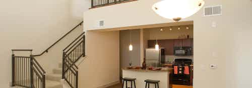 A kitchen at AMLI Inverness apartments with an island and stools and a staircase up to the bedroom and overhead lighting