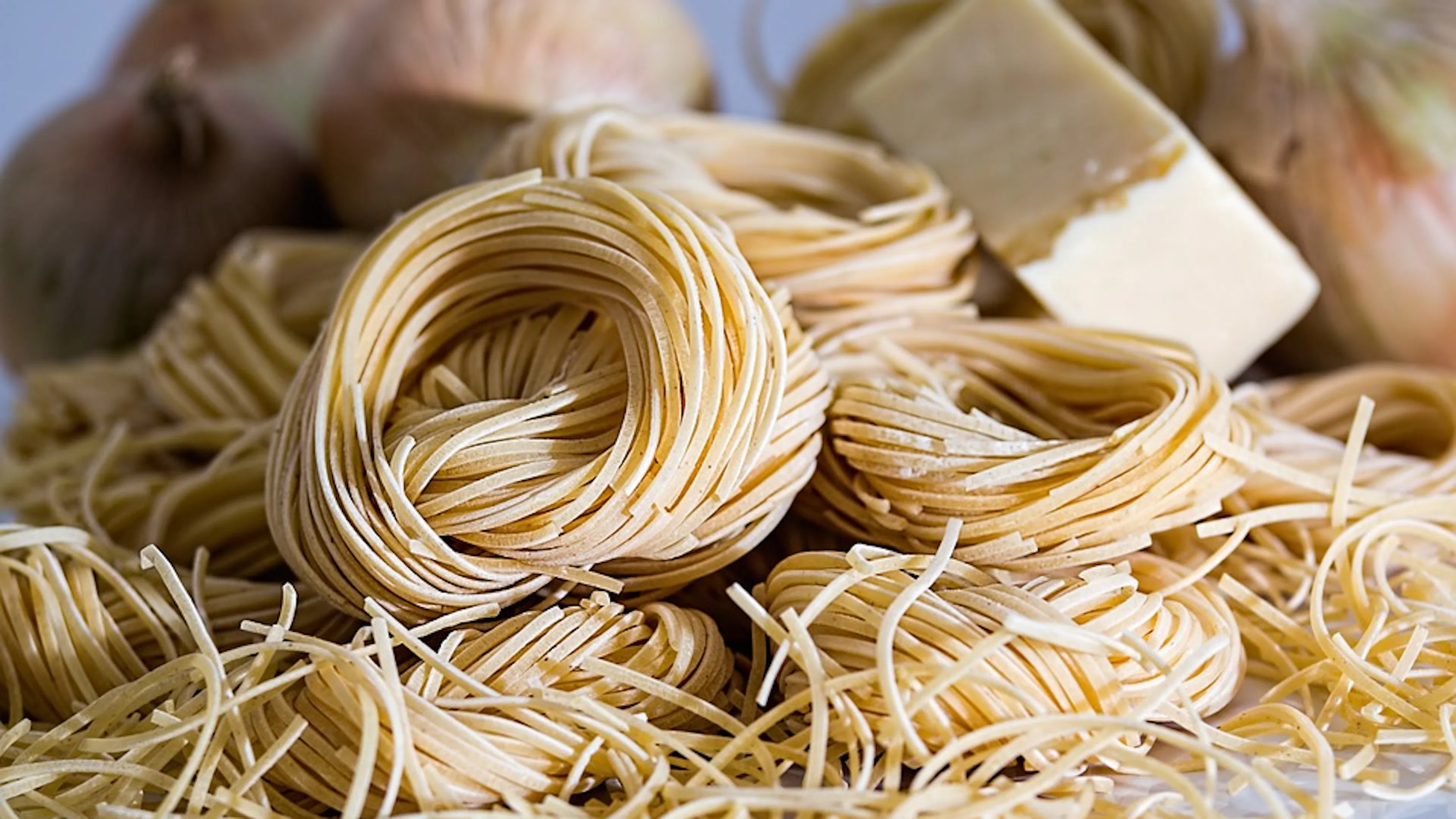 Hand made spaghetti rolled into rings with onions and butter in the background