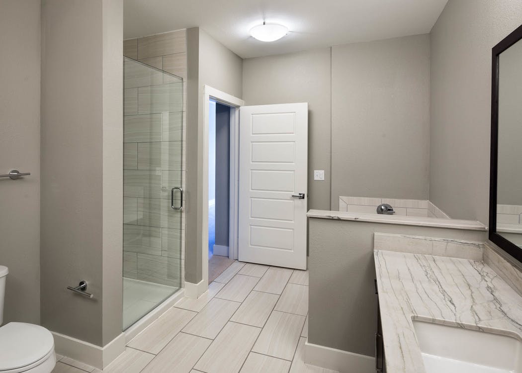 AMLI on Aldrich bathroom featuring glass door shower with white tile floor and short wall separating vanity sink from bathtub