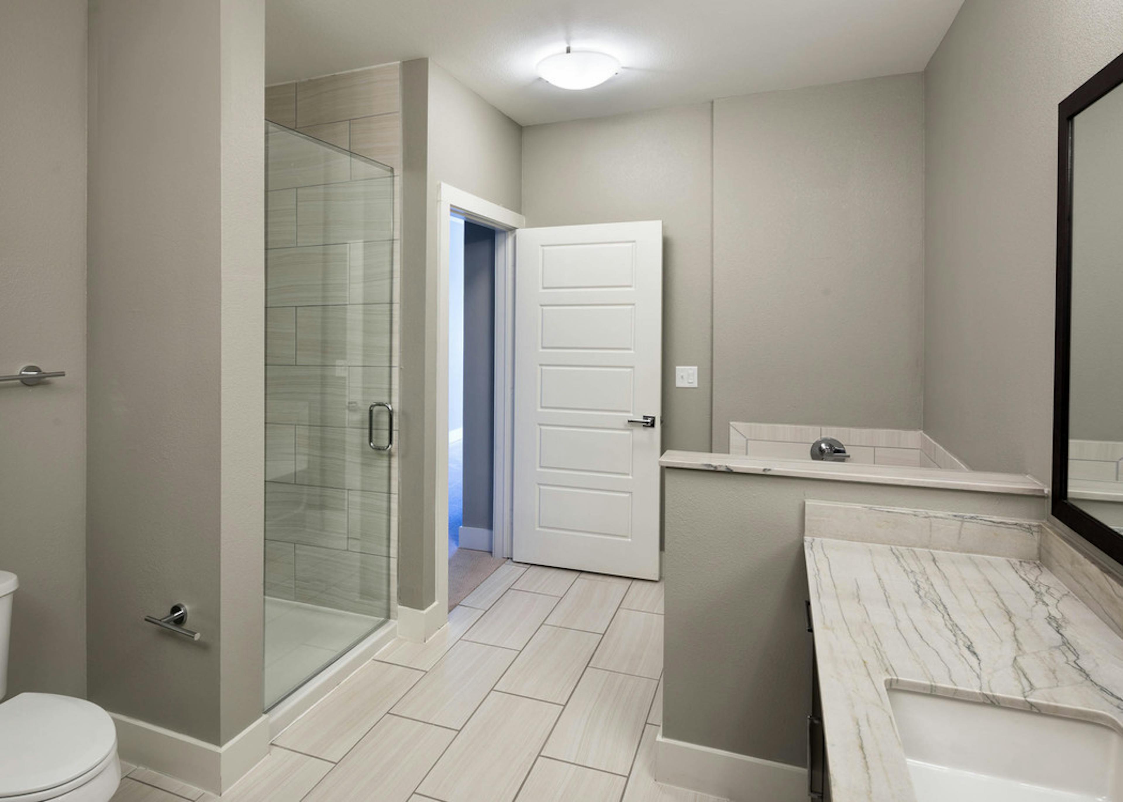AMLI on Aldrich bathroom featuring glass door shower with white tile floor and short wall separating vanity sink from bathtub