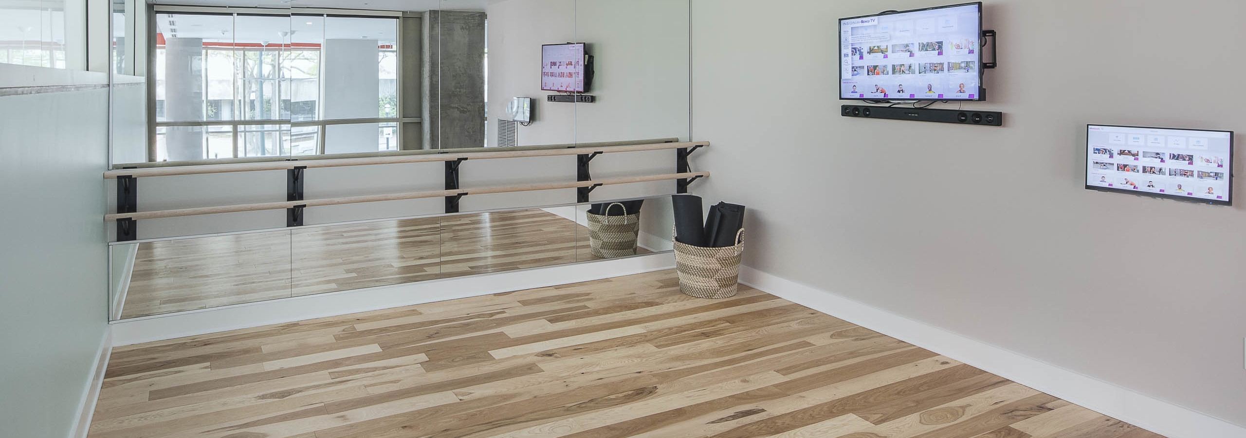 Yoga studio at AMLI Arts Center with a large wall mirror and flat screen TV with smooth wood flooring and open space