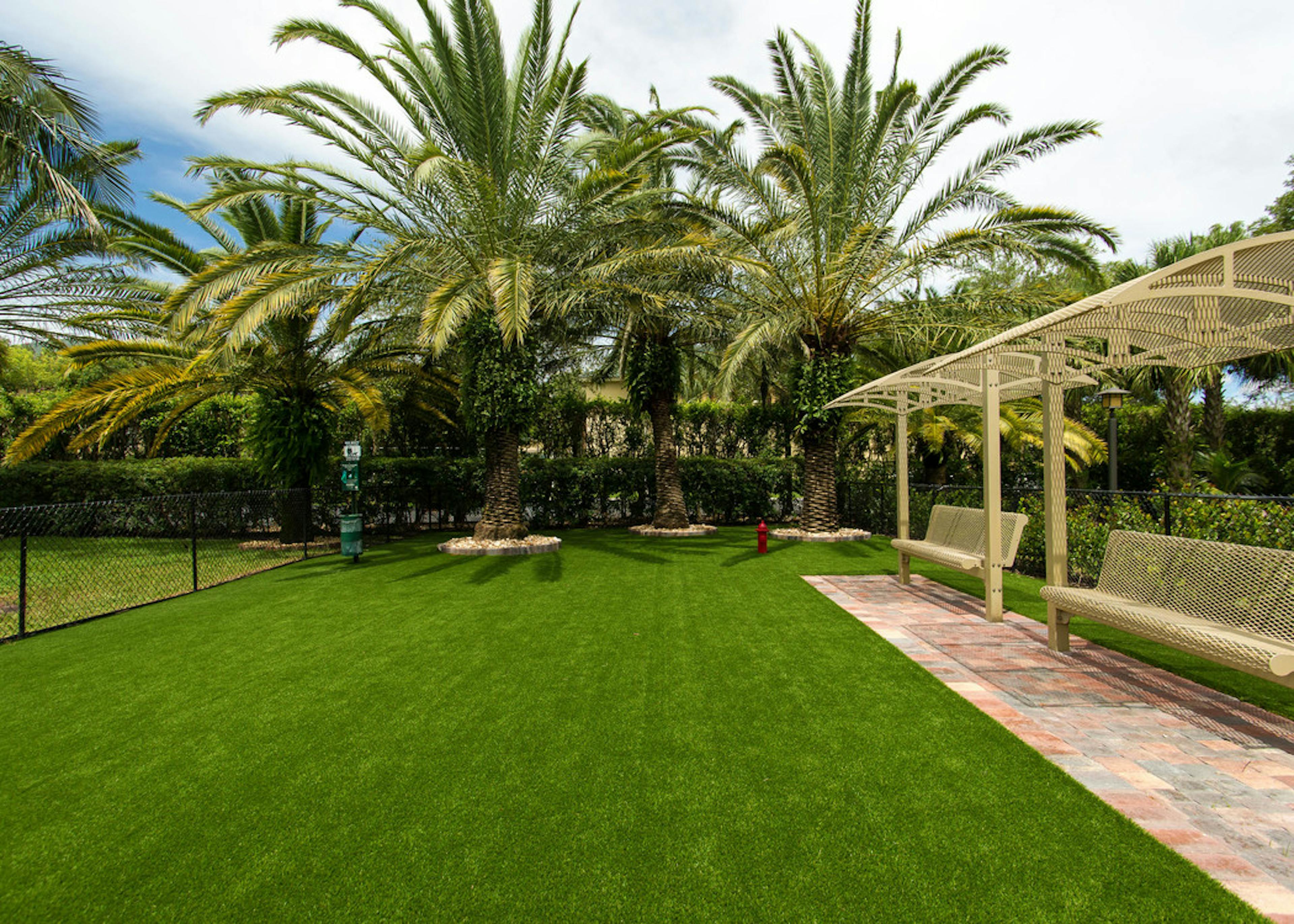 Daytime aerial view of AMLI Toscana Place expansive Paw Park with faux grass, lush landscape and covered benches