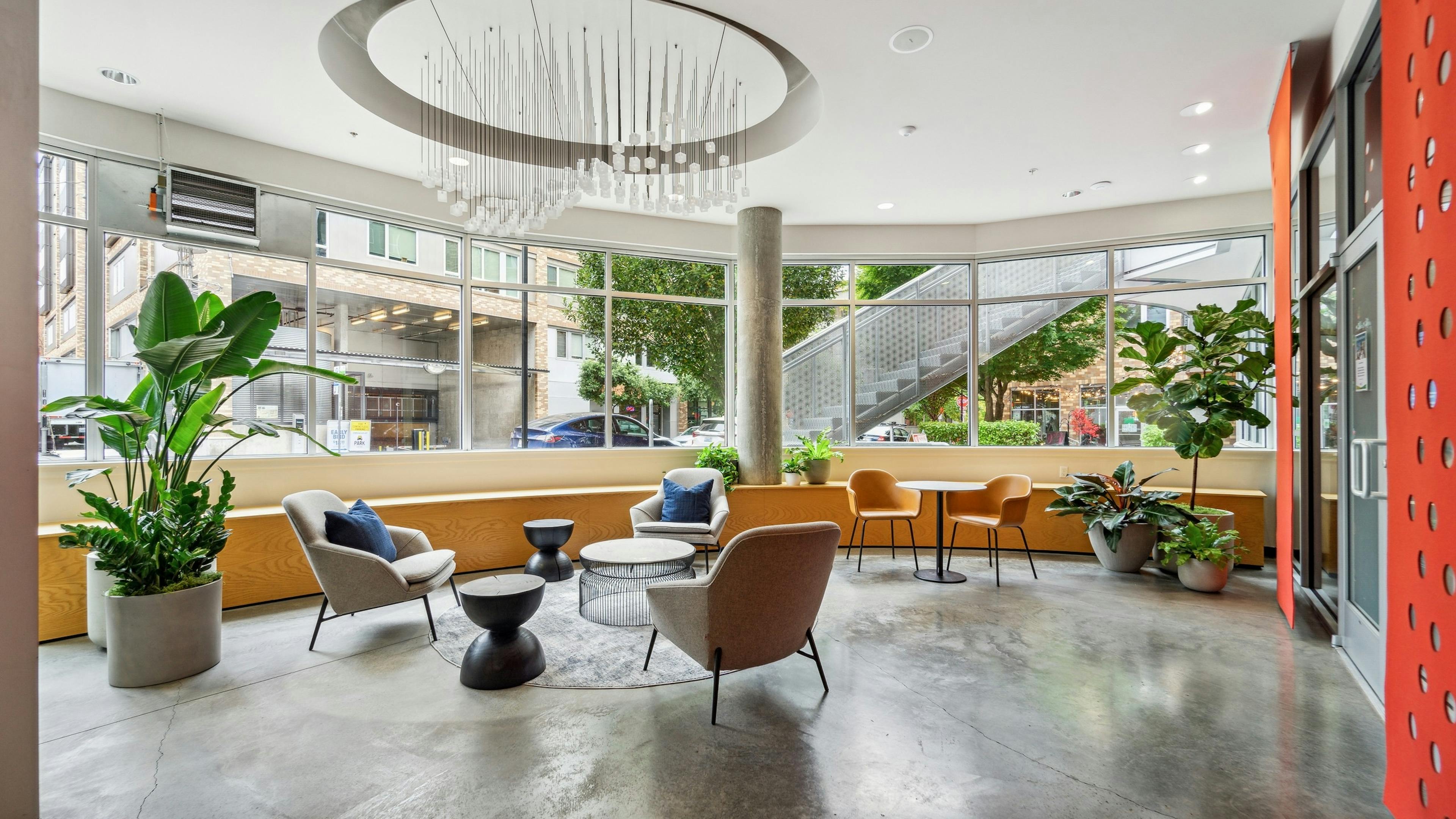AMLI South Lake Union lobby with cement flooring and multiple chairs and plants and a wall of windows and a large chandelier
