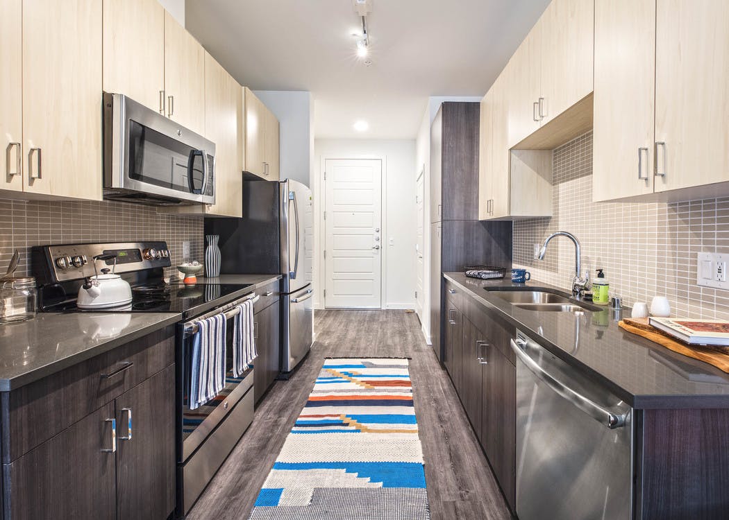 Interior view of an AMLI Wallingford apartment kitchen with two tone light and dark cabinets grey quartz counter tops and stainless steel appliances