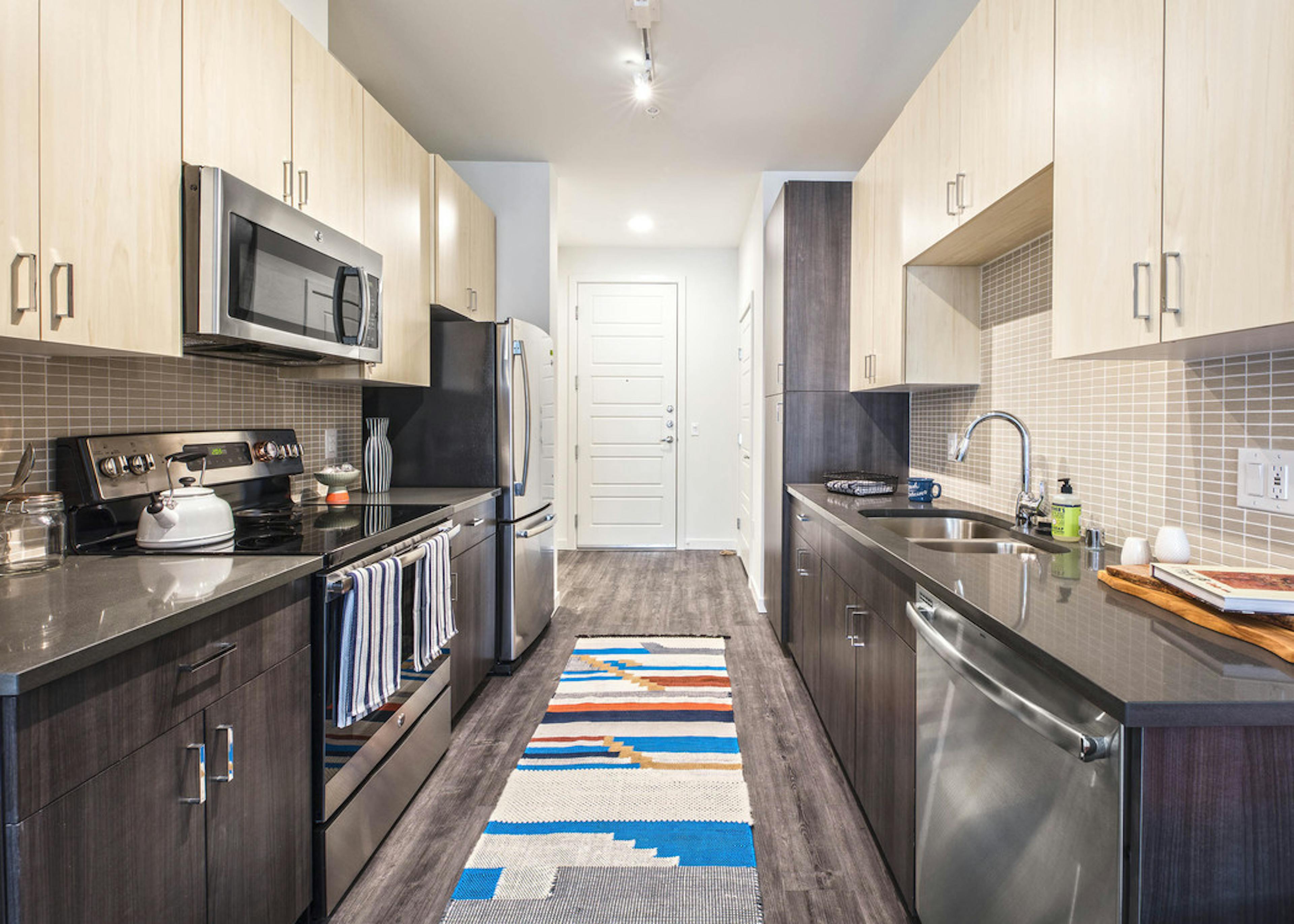 Interior view of an AMLI Wallingford apartment kitchen with two tone light and dark cabinets grey quartz counter tops and stainless steel appliances  