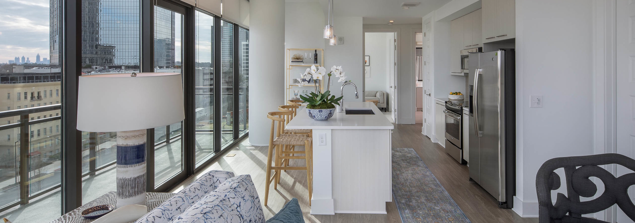 Open concept kitchen and living area at AMLI 3464 with windows along the entire back wall and wood flooring with white walls
