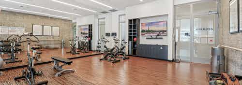AMLI Arc Zen Den with spin bikes and weightlifting bench on wood grain floor and dumbbells and TV mounted over dark cabinet