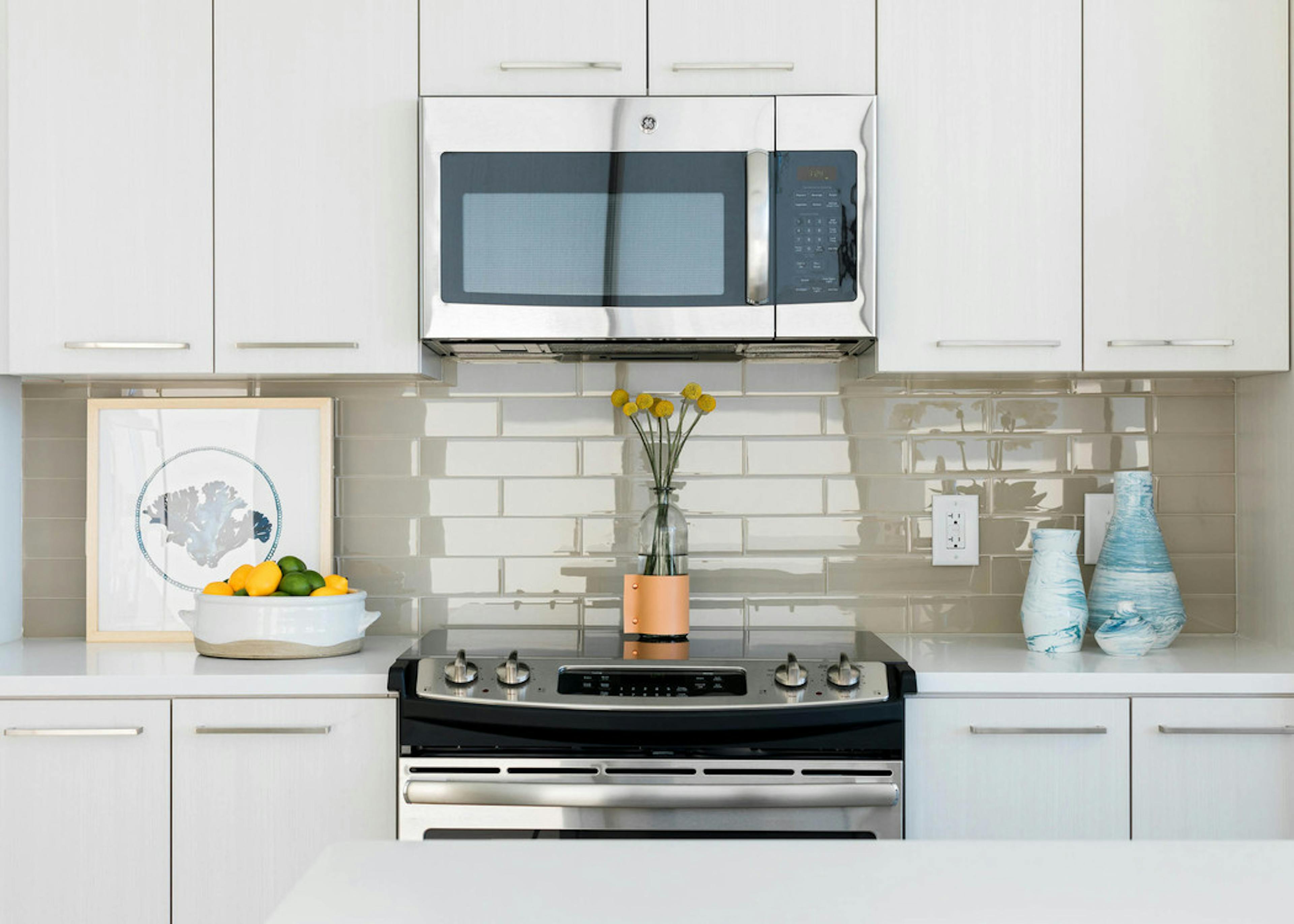 Close up of countertops at AMLI 3464 with a beige tile backplash and a decorative fruit bowl with a vase of yellow flowers