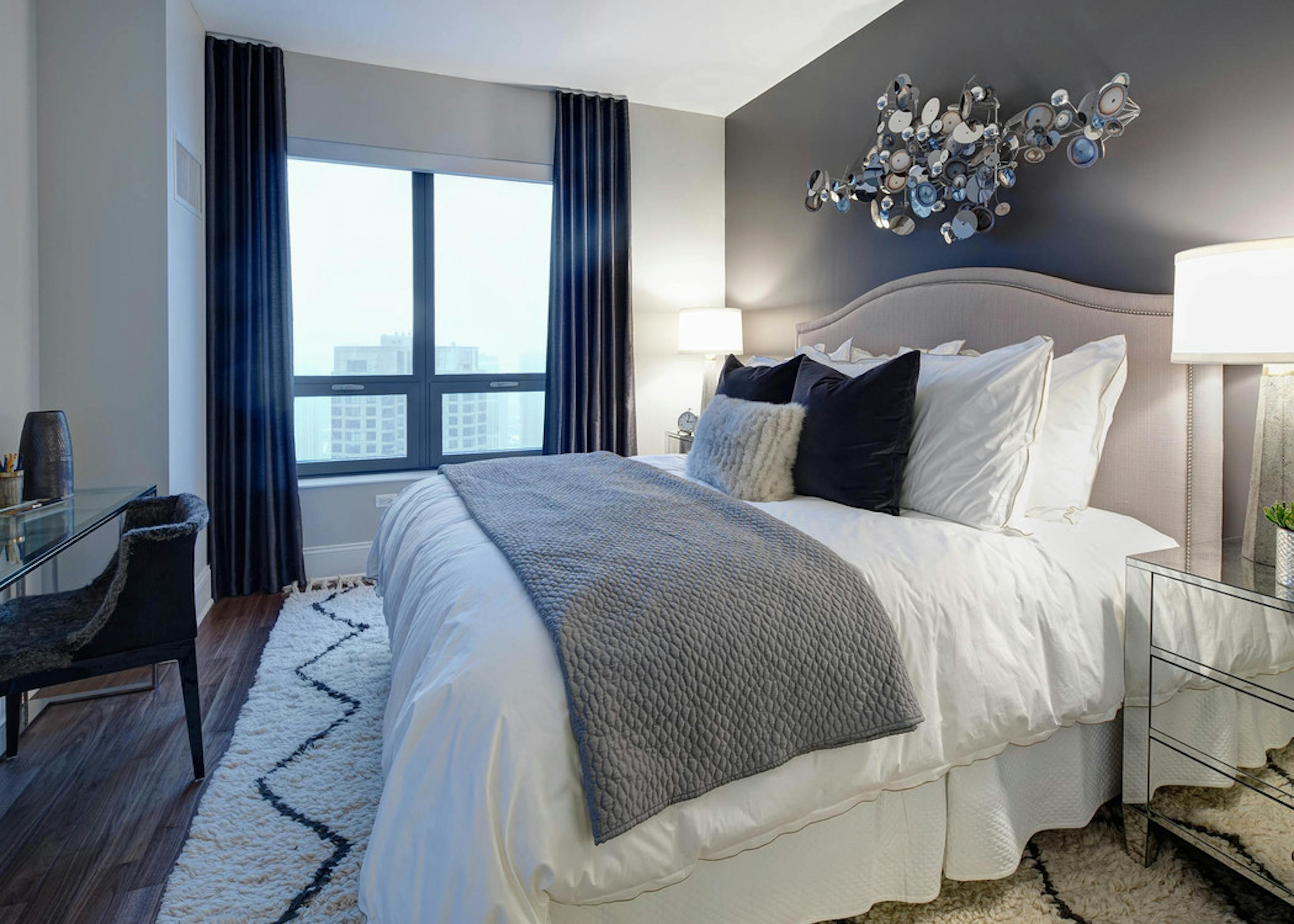 Penthouse bedroom at AMLI River North with a dark accent wall that a beige heardboard is leaning against with white bedding