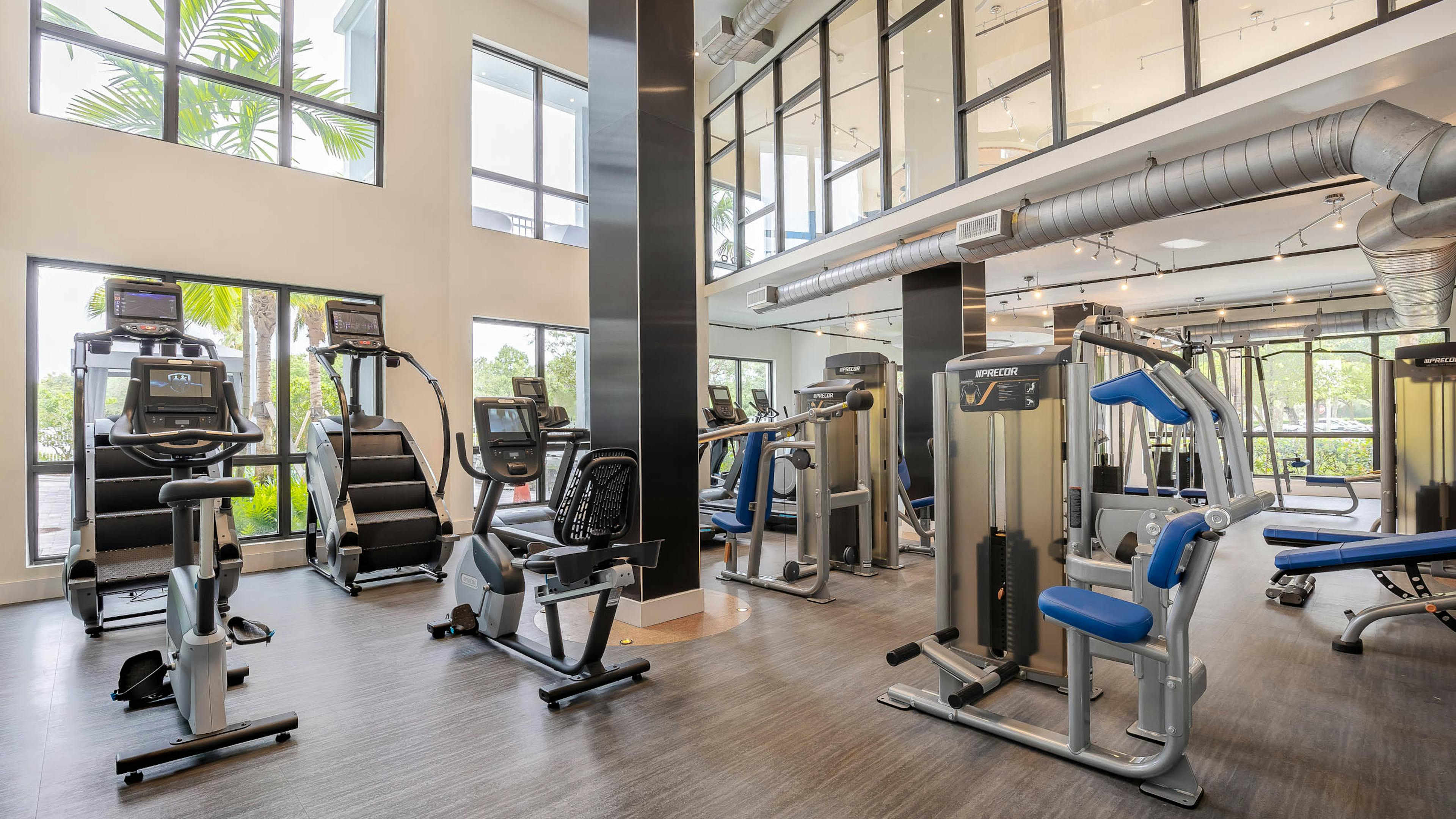 Interior view of the fitness zone at AMLI Park West apartments with cardio and weight machines and window views 