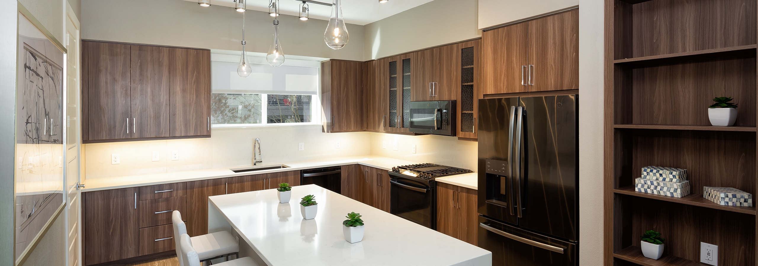 AMLI South Shore island kitchen with a built in dark wood shelf and cabinets with quartz countertops and white barstools