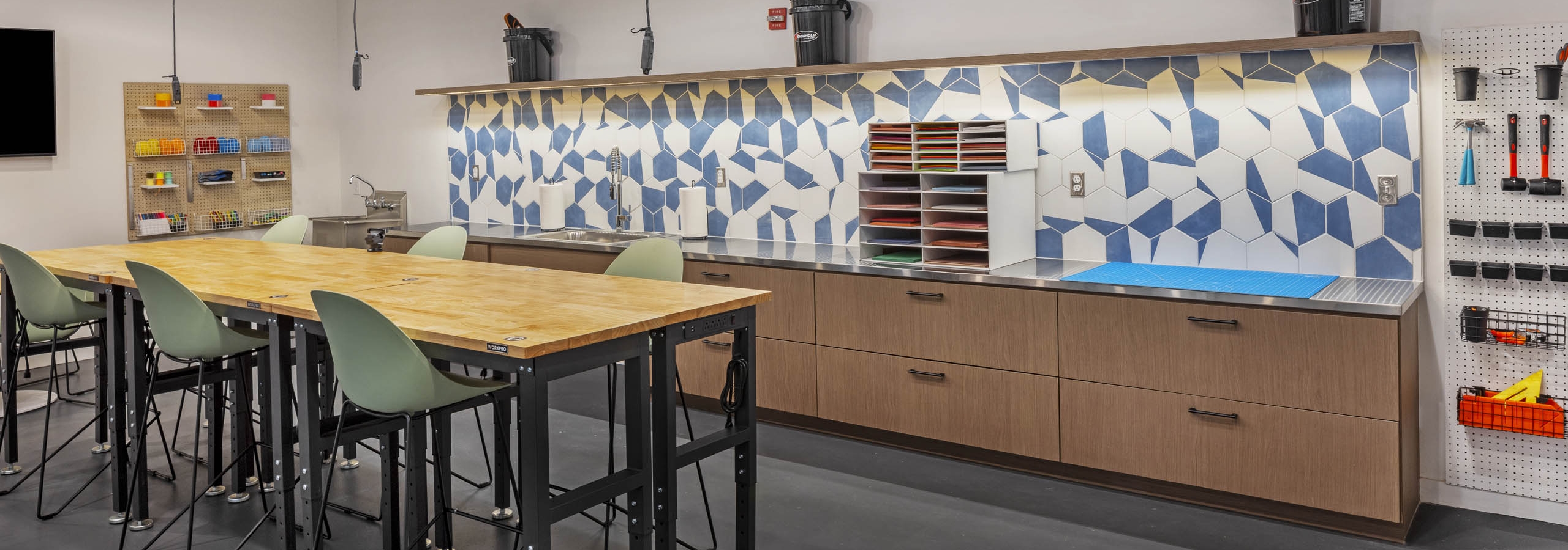 AMLI on 2nd maker space with bar height wood worktable with green chairs and counter space with blue and white geometric tile