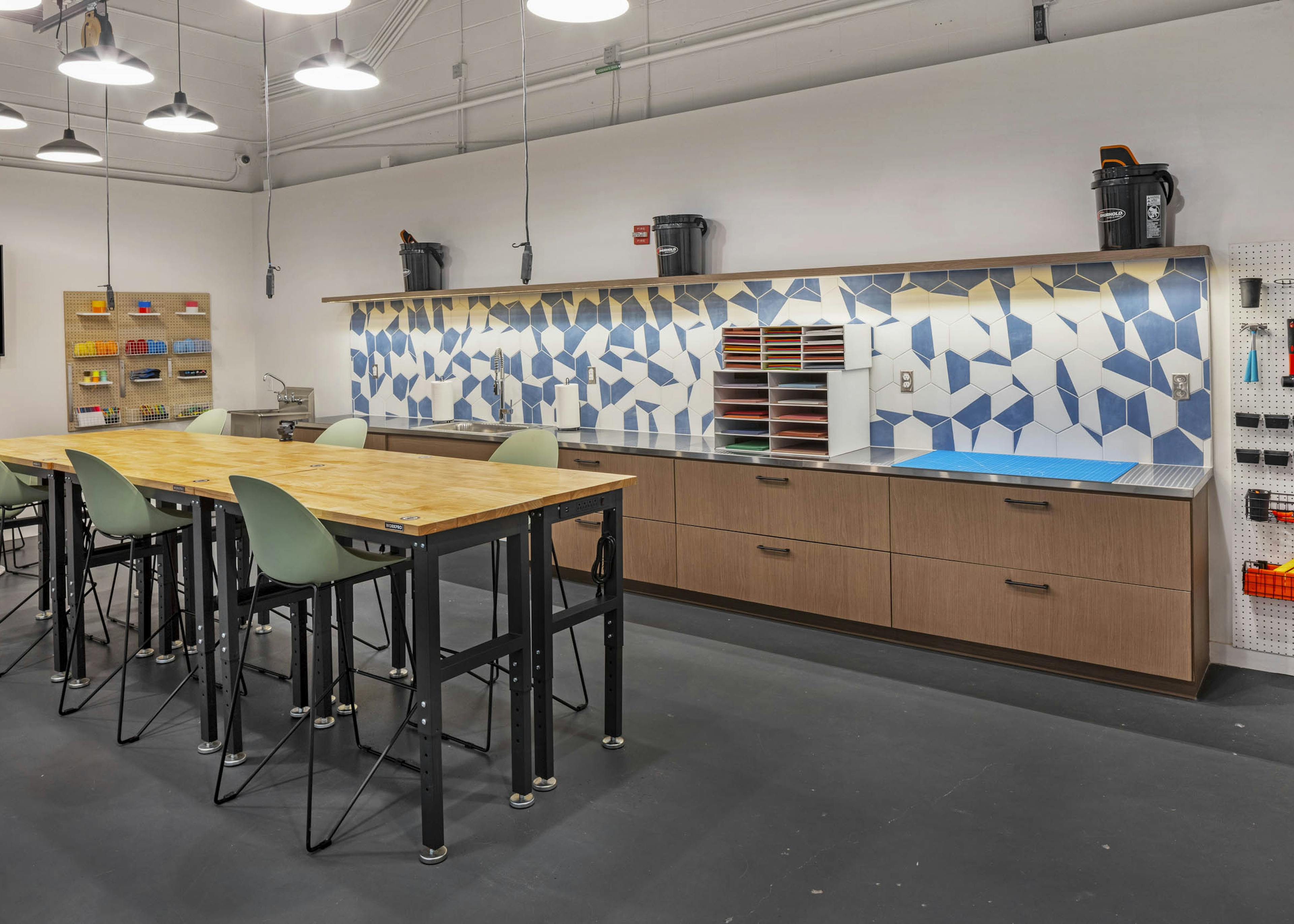 AMLI on 2nd maker space with bar height wood worktable with green chairs and counter space with blue and white geometric tile