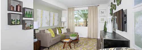 Interior of AMLI Spanish Hills apartment living room with sofa facing big screen TV and large window with sheer tan curtains