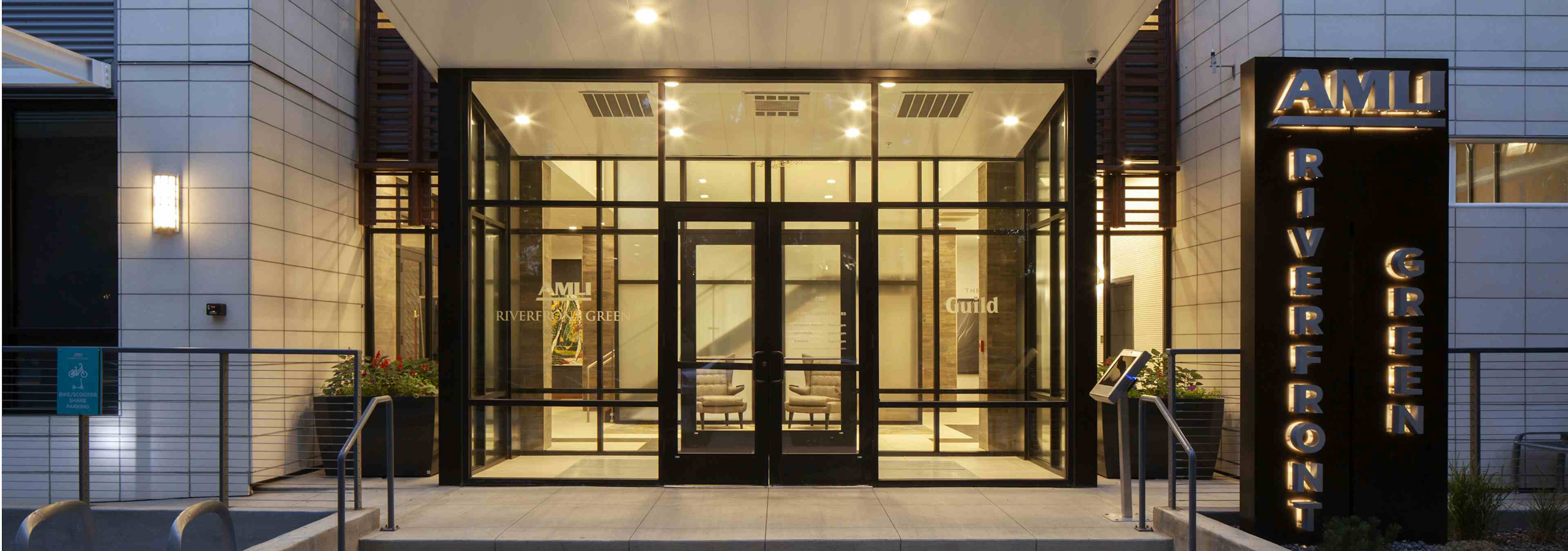 Night time exterior of AMLI Riverfront Green apartment building main entrance with sidewalks and brightly lit signage